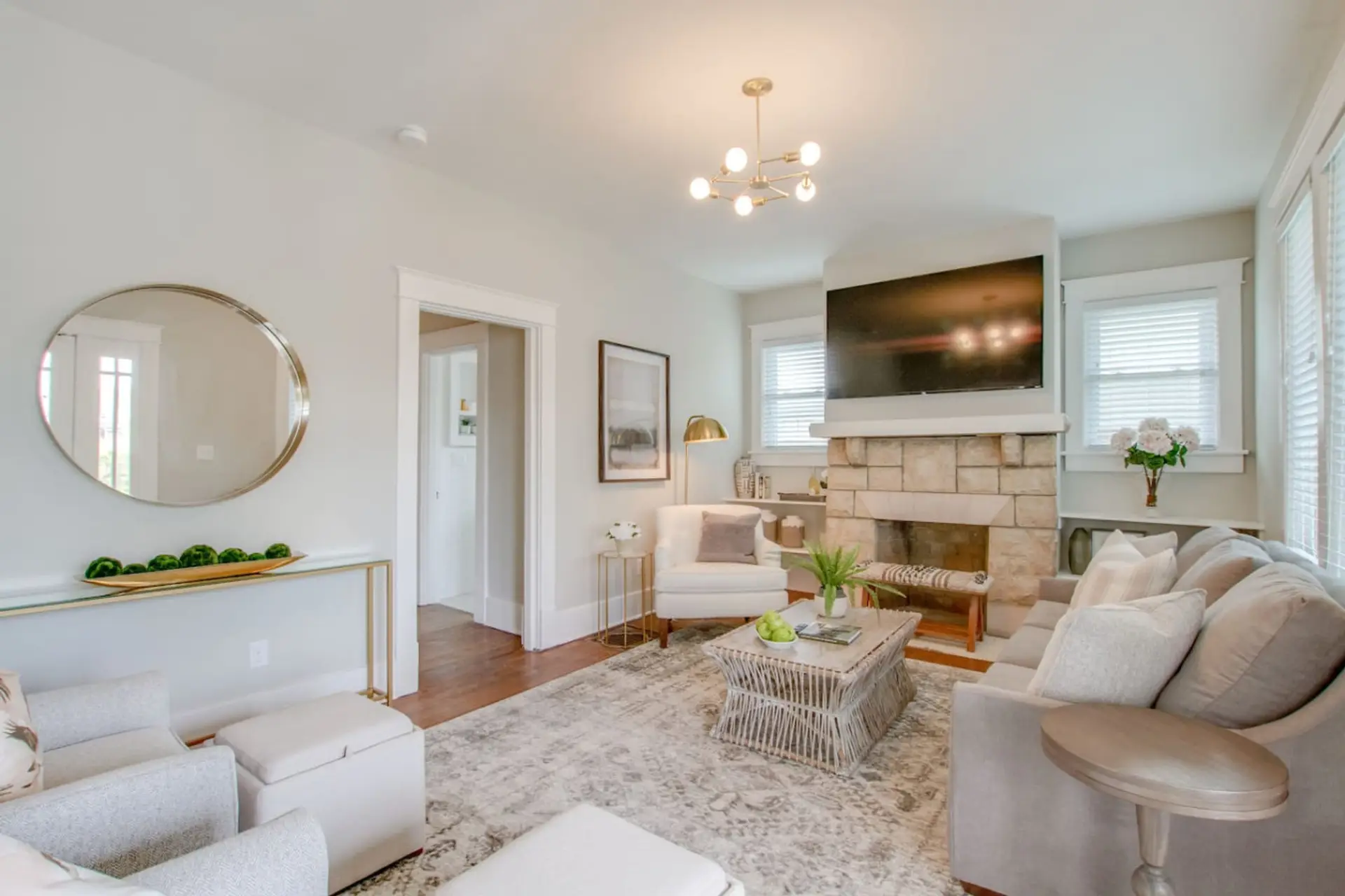 Living room with cream sofa, fireplace with TV, round mirror, pendant lights, and plants