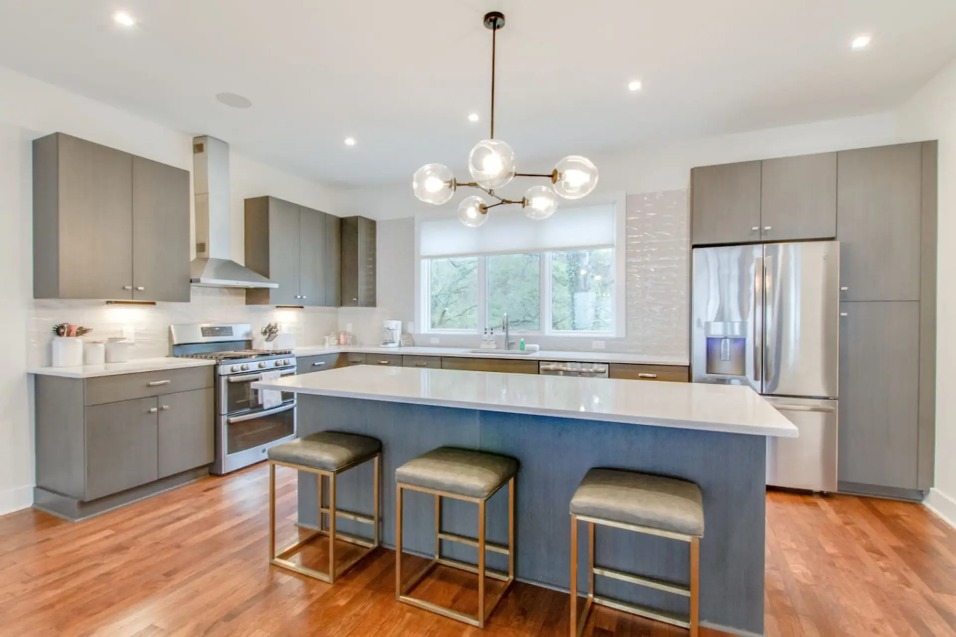 Modern kitchen with gray cabinetry, large island with bar stools, chandelier, and brick backsplash