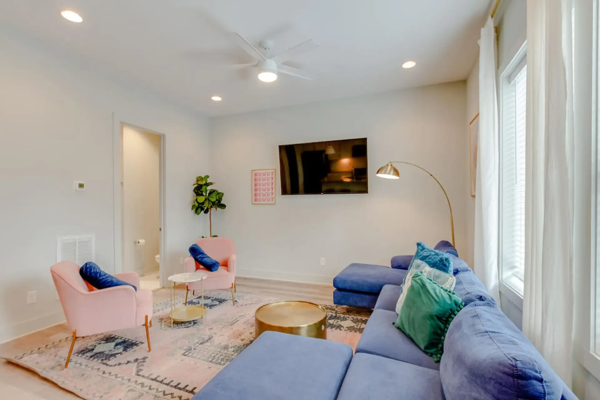 The bright living room with blue sectional, pink chair, and large TV makes group hangouts easy.