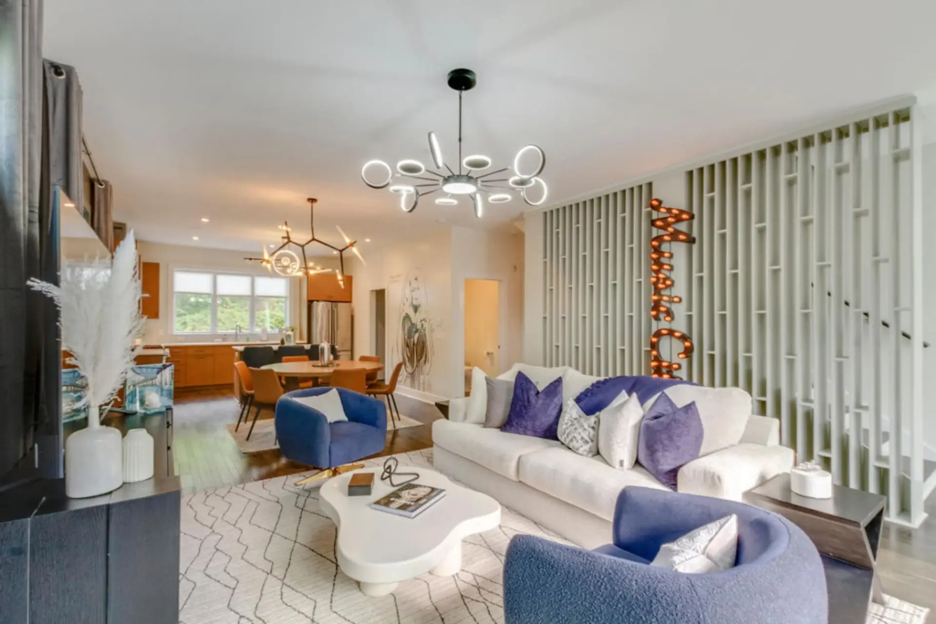 Open living room with white sofa, blue accent chairs, and modern globe chandelier
