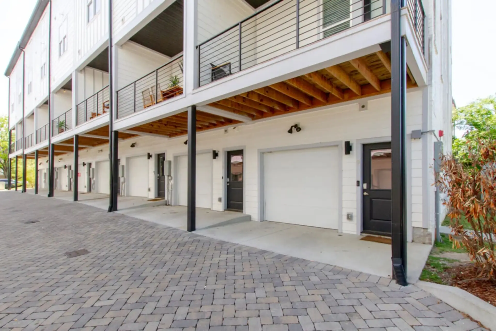 Exterior courtyard with covered carport, wood-paneled ceiling, garages, and brick pavement