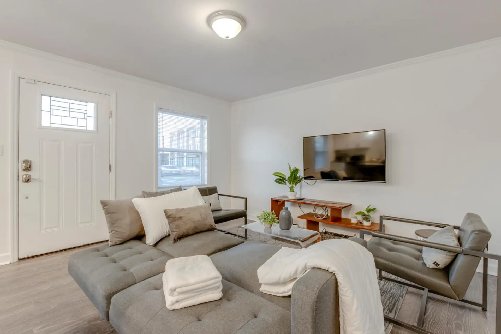 Living room from a wider angle showing the front door, gray sofa, and TV console