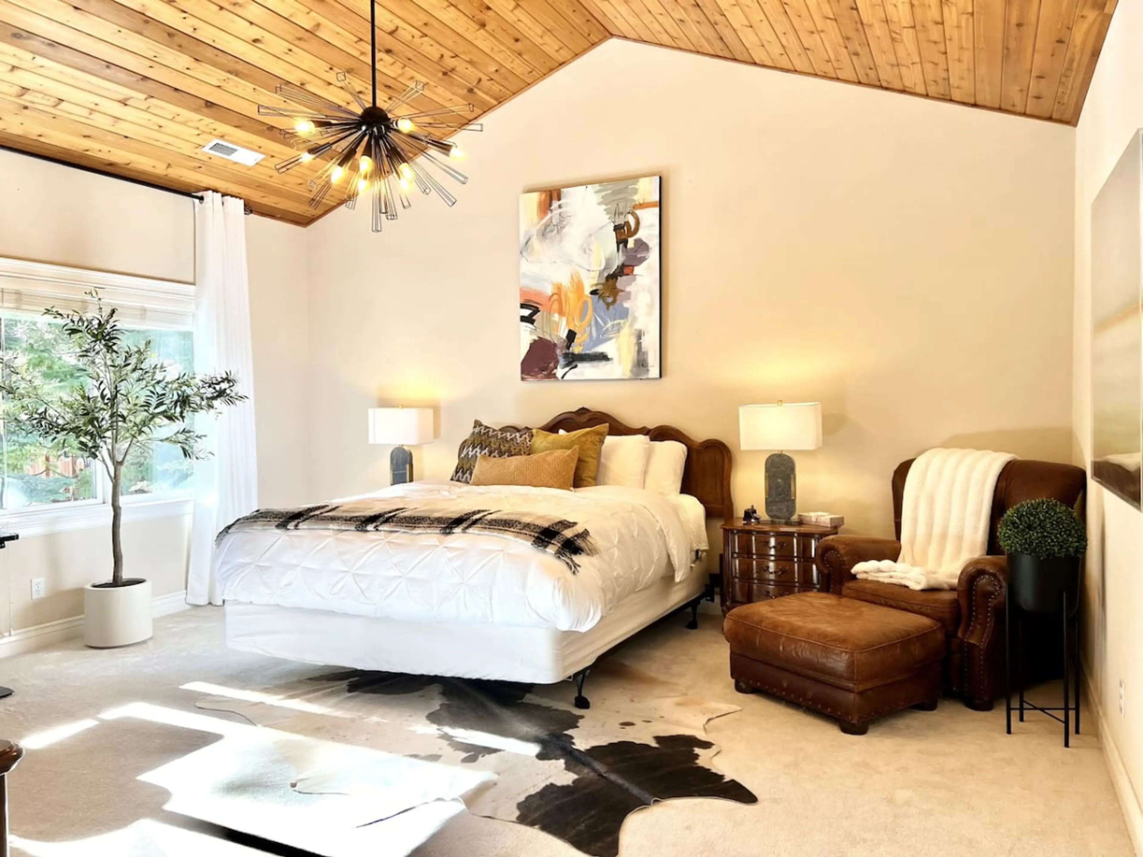 Large upstairs master bedroom with vaulted wood paneled ceiling, king bed, a lounge chair and a work desk looking out into the forest, window blinds, curtains, dresser and wifi TV