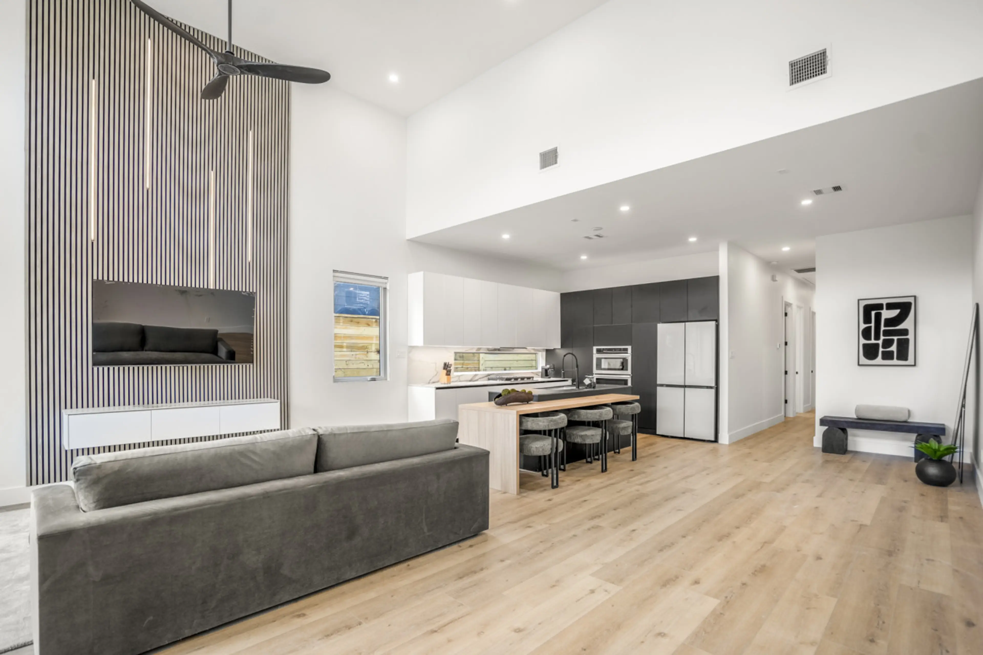 A bright, airy living space featuring a sleek kitchen, cozy lounge area, and modern wood-accented media wall.