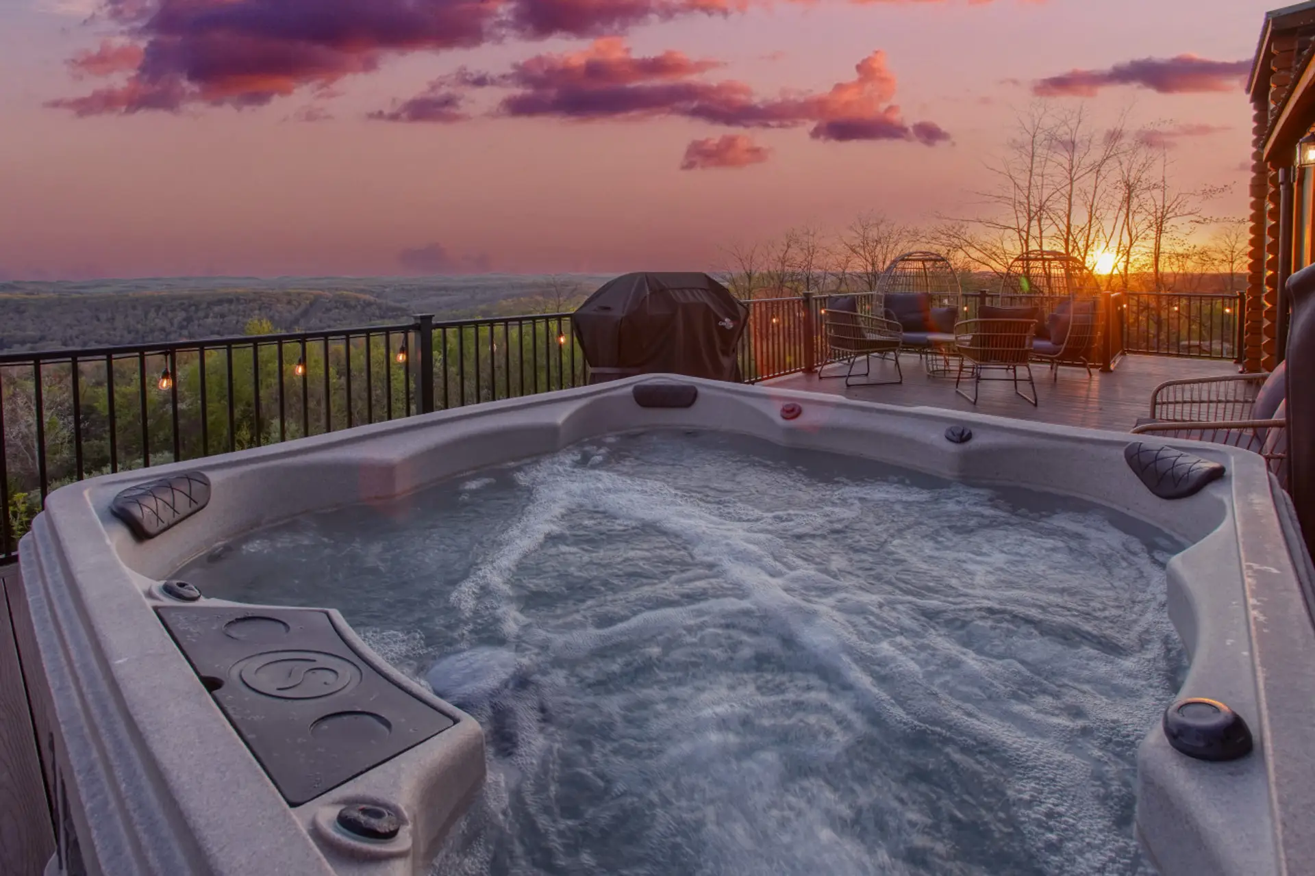 Outdoor hot tub on a deck with patio furniture and grill, overlooking view