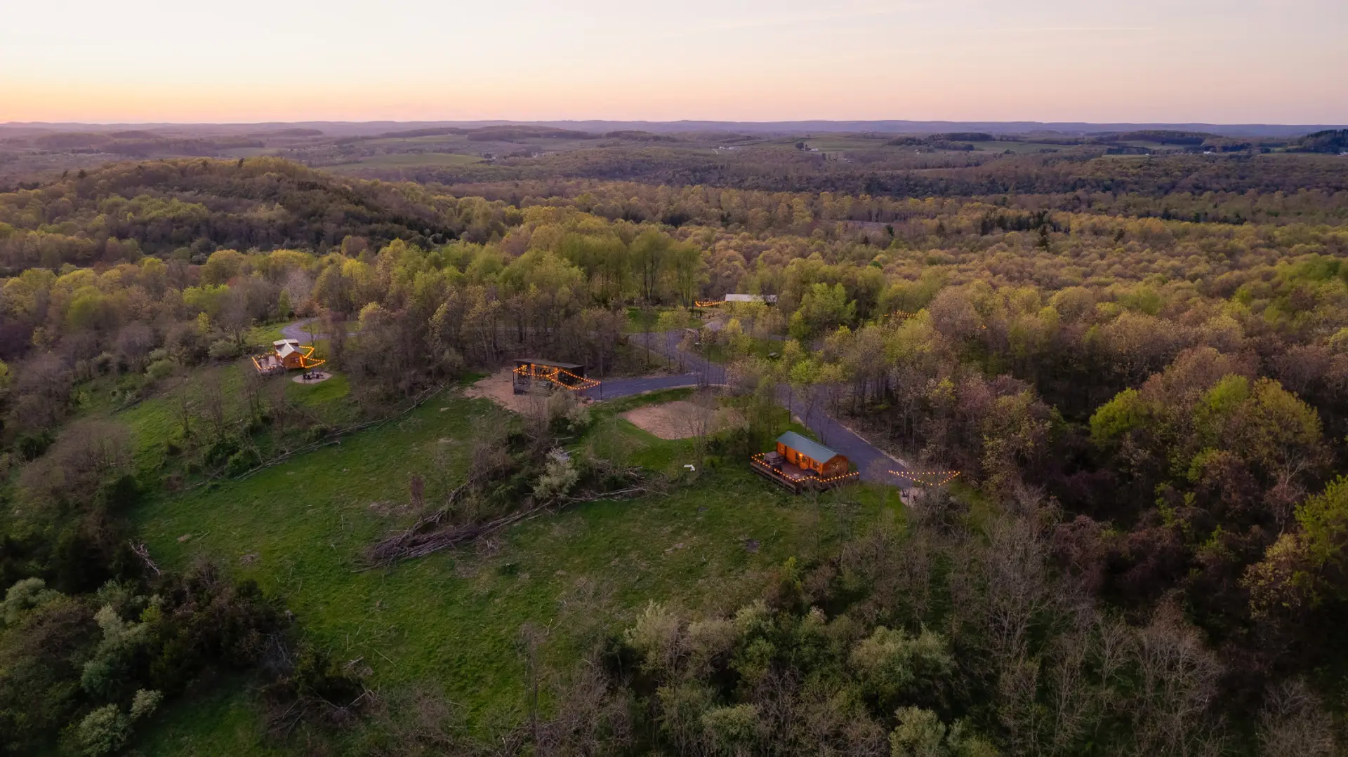 Aerial view at sunset of cabins nestled in a lush, rolling forest