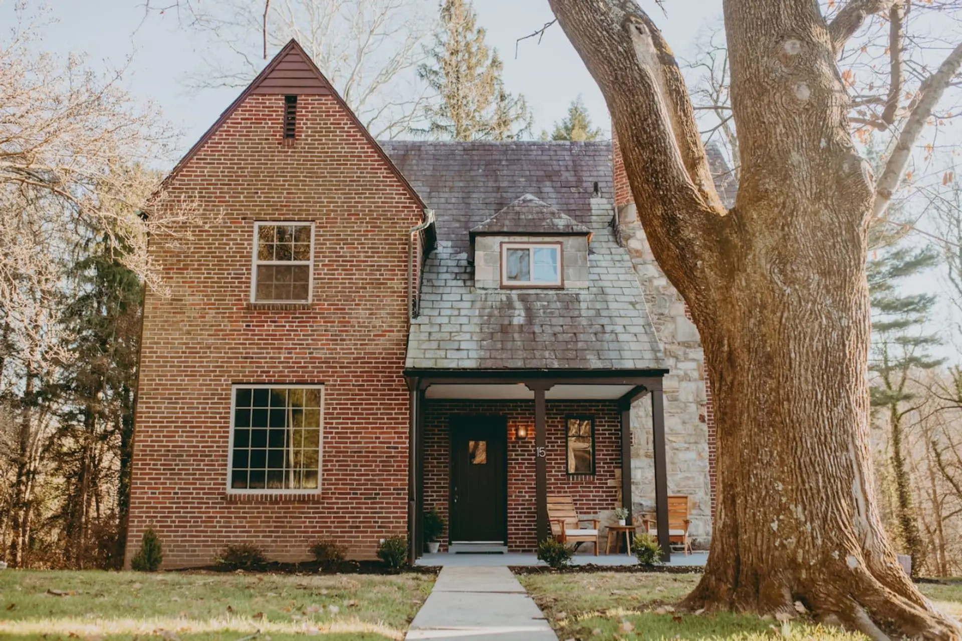 Brick house with a large front tree, and a small porch with seating