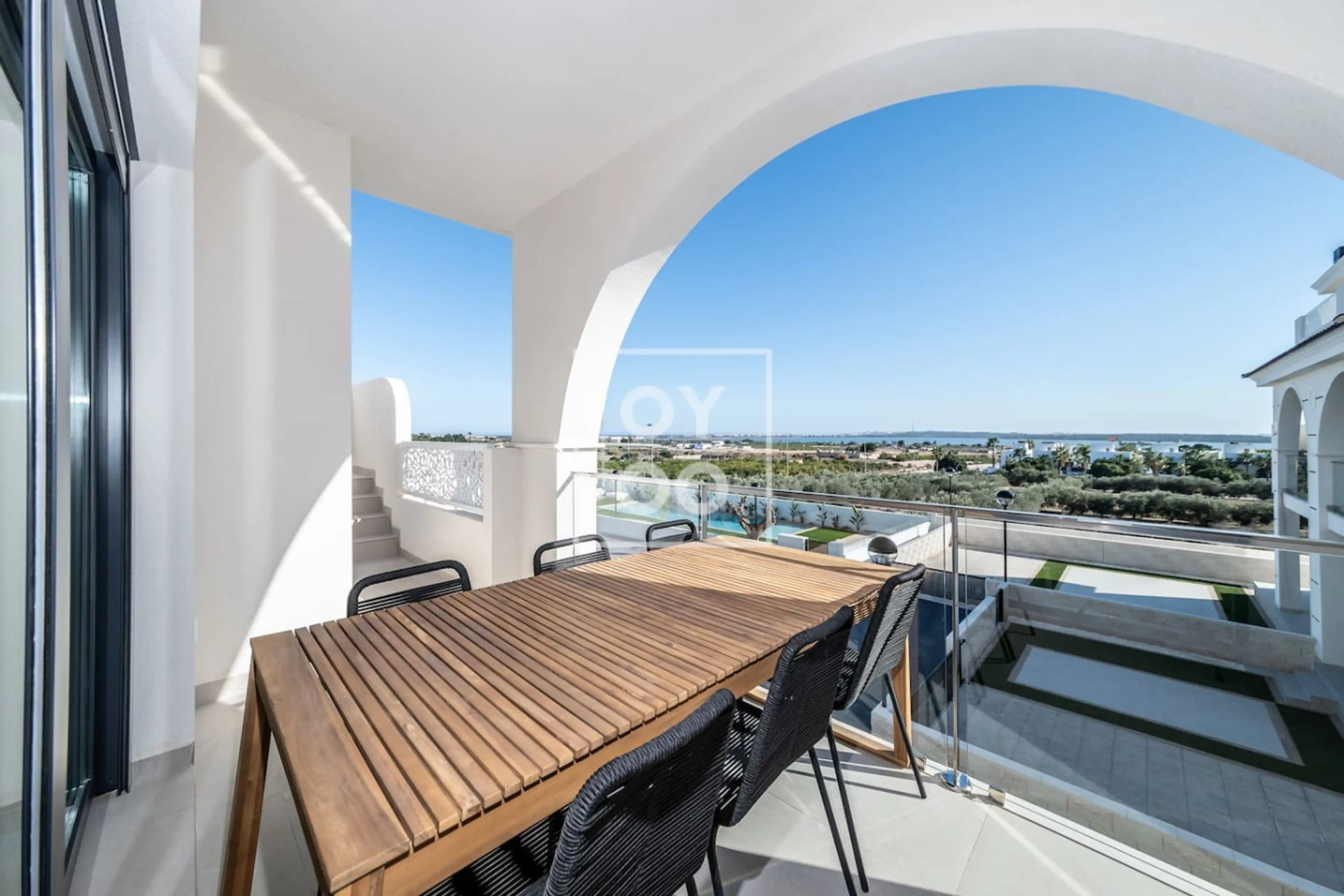 Spacious balcony features a wooden dining table with seating for six under a graceful arch, perfect for al fresco meals. Enjoy panoramic sea and pool views as you relax in this bright outdoor lounge area. 🌊🍽️☀️
