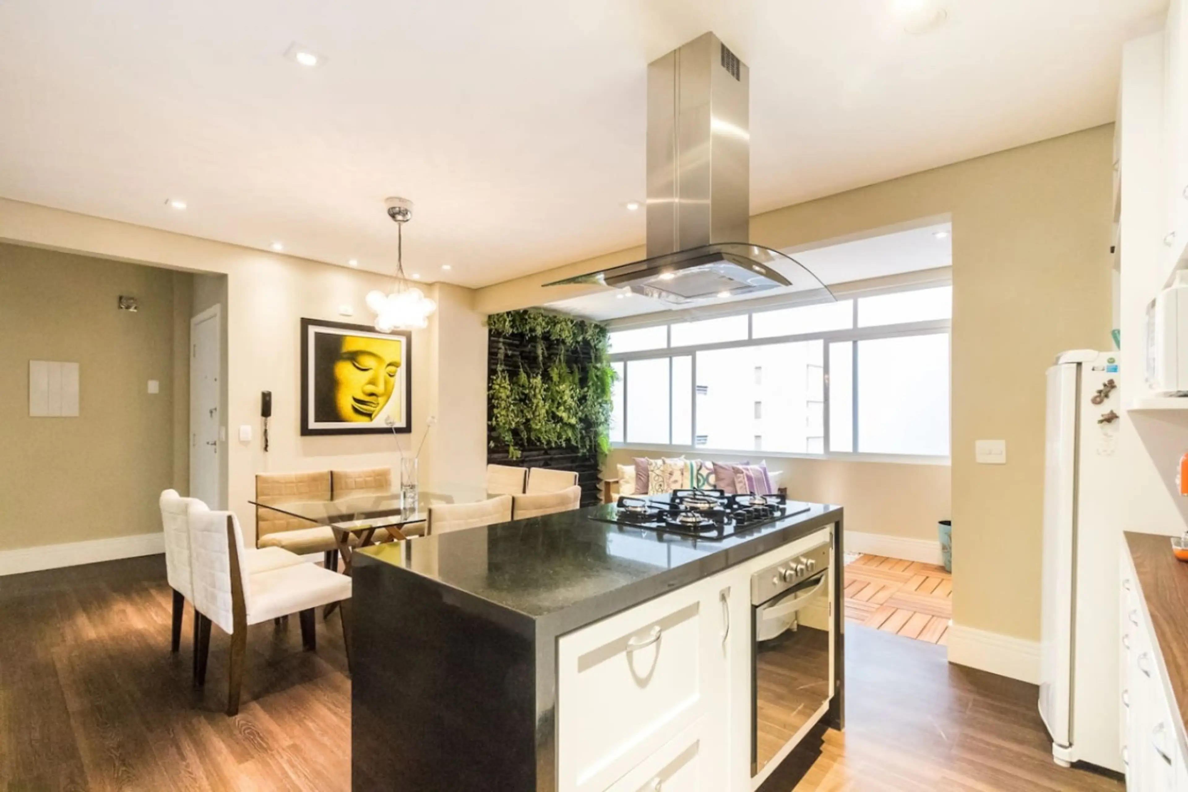 Ambiente integrado com cozinha moderna em ilha, sala de jantar elegante e parede verde, garantindo praticidade, estilo e aconchego em um só espaço.