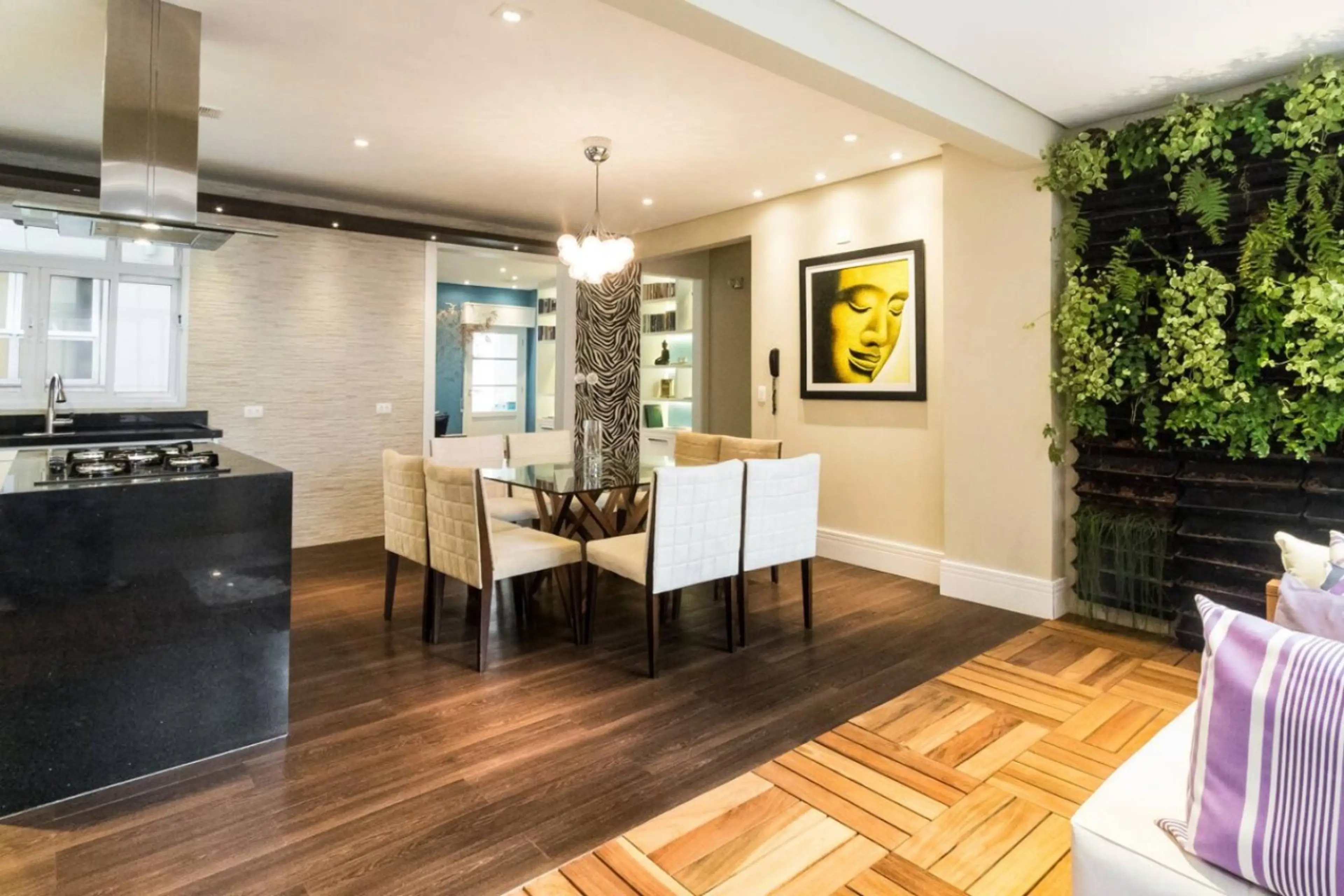 Sala de jantar sofisticada integrada à cozinha, com mesa para seis pessoas, decoração moderna e parede verde natural que traz frescor ao ambiente.