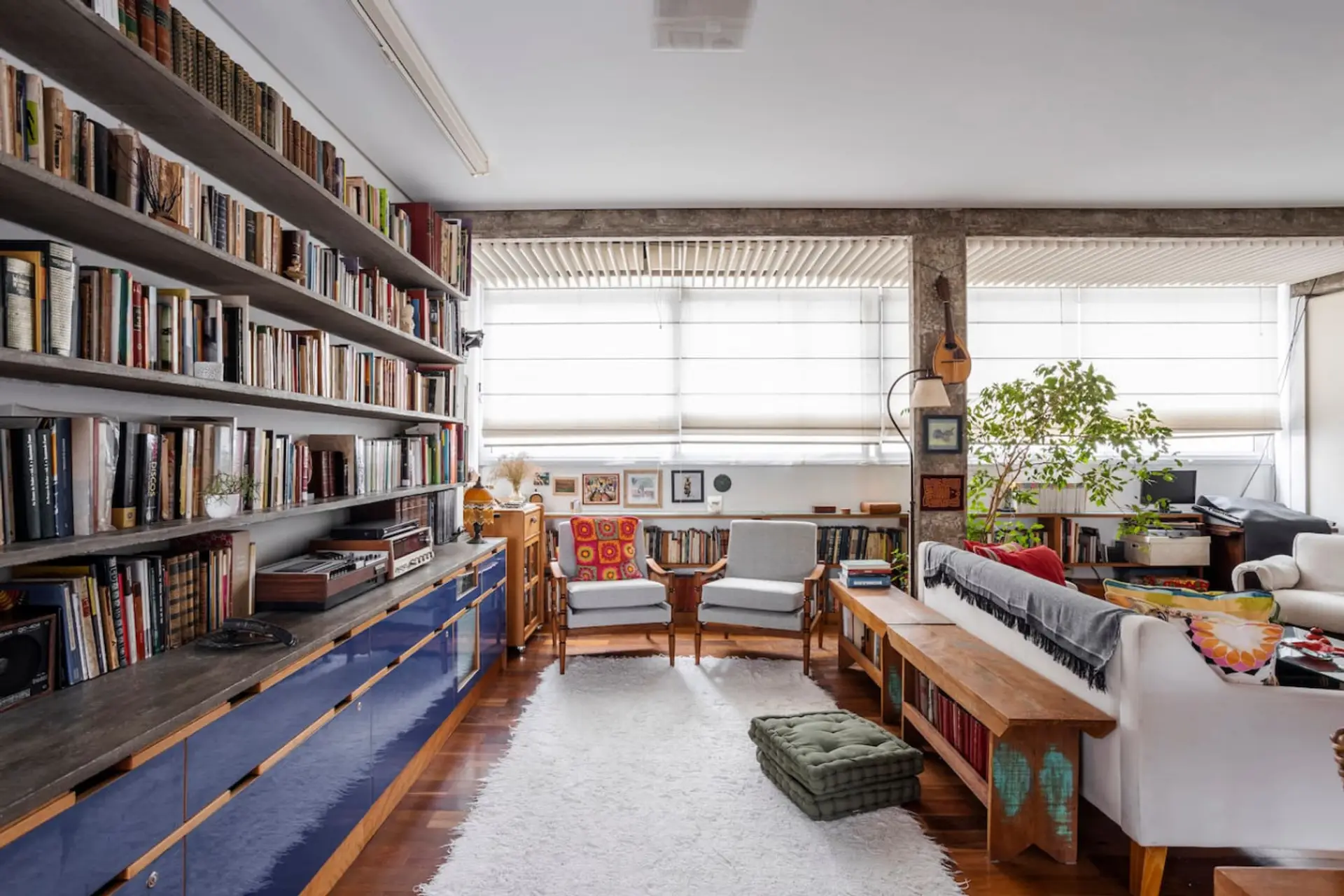 Uma sala acolhedora e cheia de charme, com estantes repletas de livros, móveis de madeira, poltronas confortáveis e uma iluminação natural abundante.