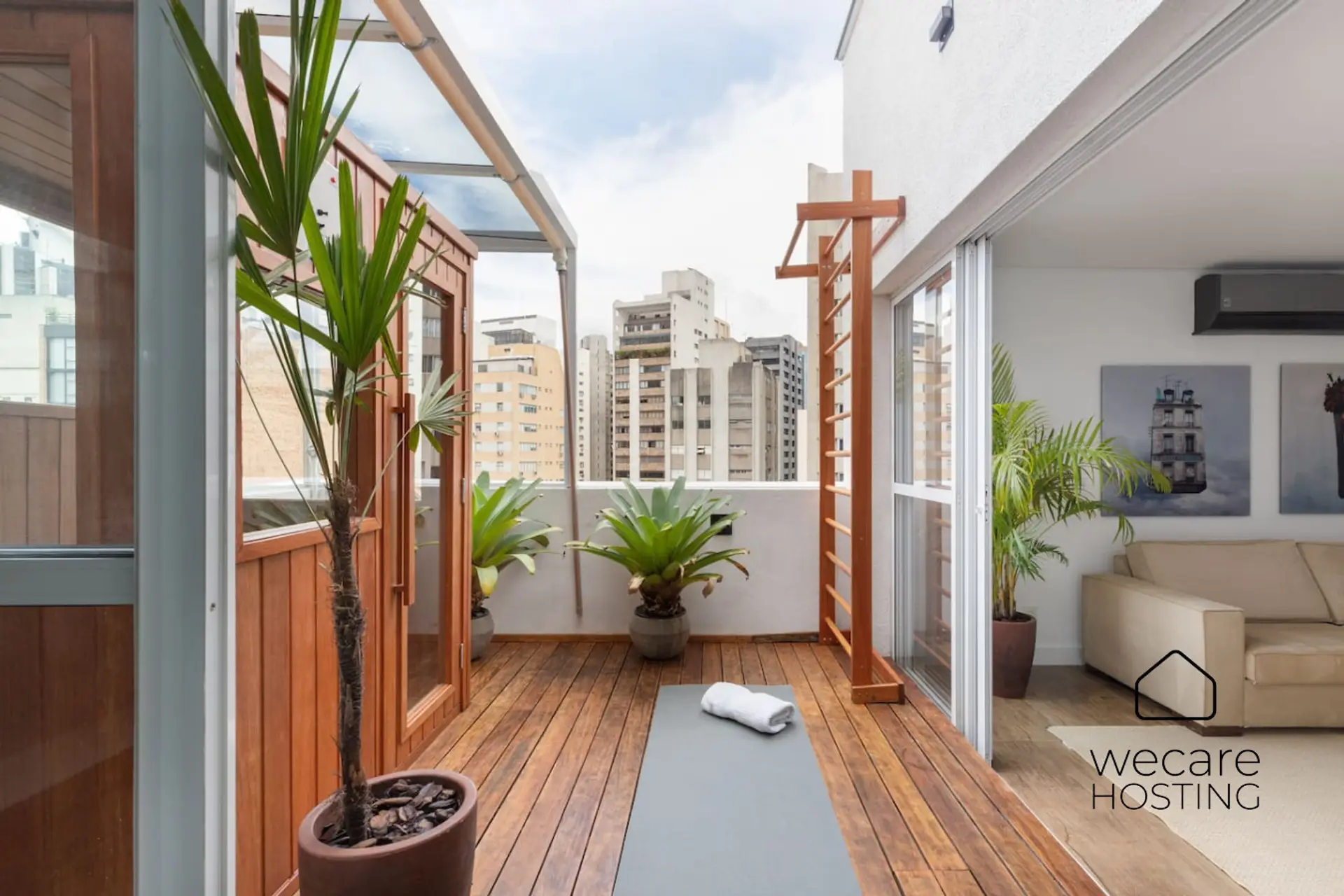 Terraço com piso de madeira, espaço para prática de yoga e espaldar funcional. Integração perfeita entre bem-estar, sauna e sala, com skyline paulistano ao fundo.