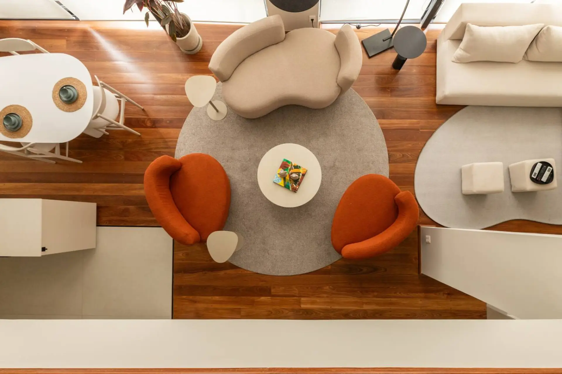 Vista aérea da sala de estar com design contemporâneo, poltronas em tons quentes, tapetes sobrepostos e iluminação natural que valoriza o ambiente.