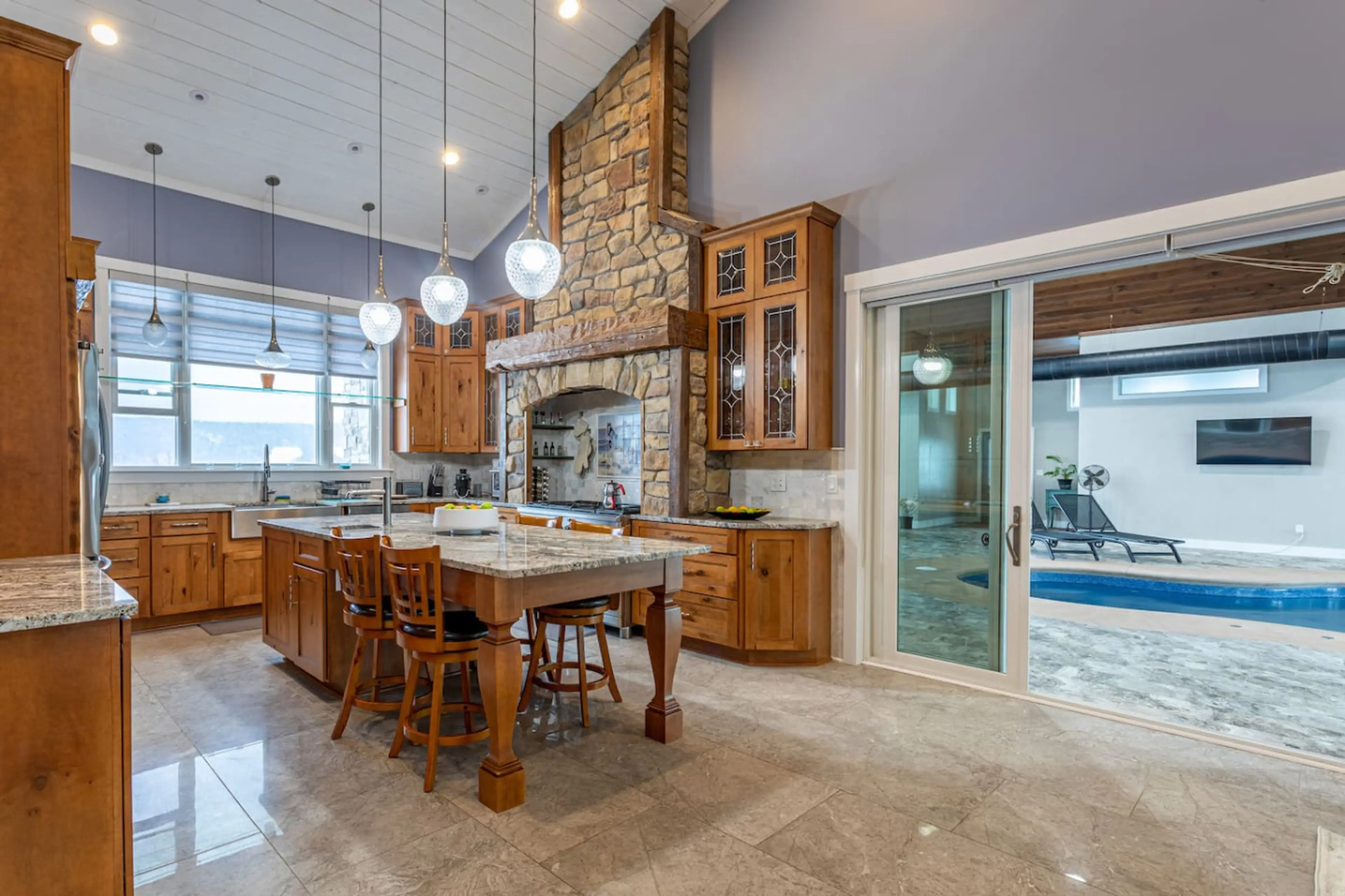 Kitchen island with bar seating and stone range hood, open to the indoor pool room through sliding glass doors