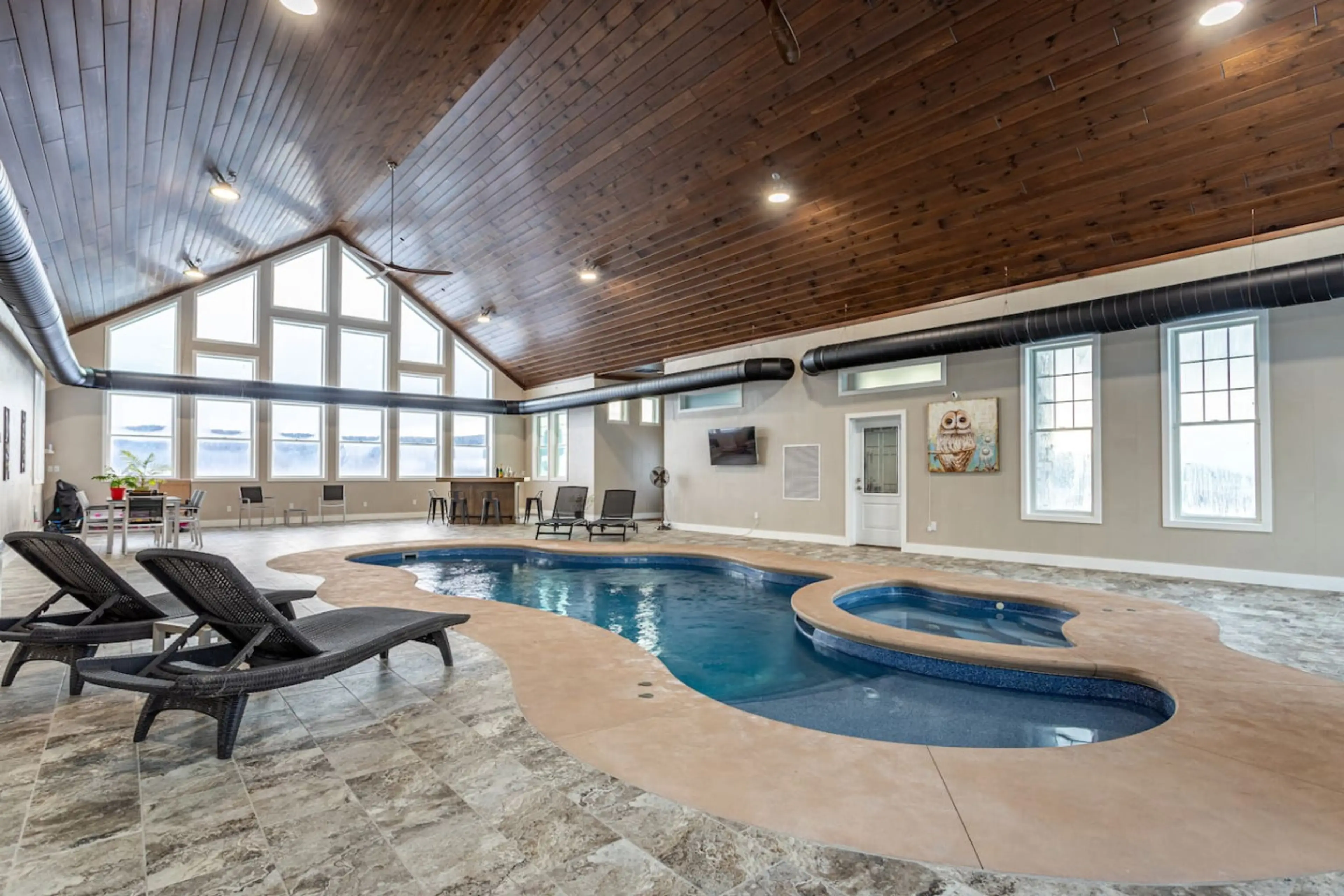 Indoor pool and adjoining sauna with vaulted wood ceiling, stone fireplace, and lounge chairs