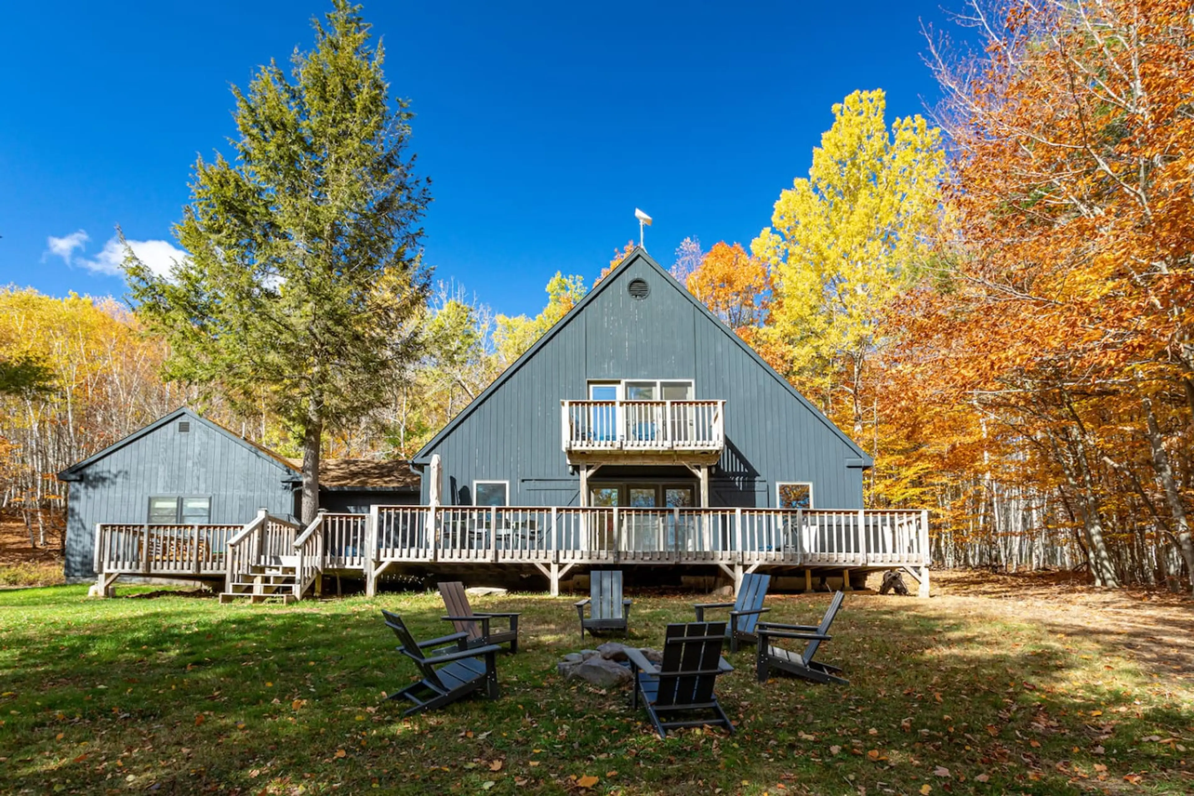 Cottage exterior with multi-level decks, fire pit, Adirondack chairs, and fall foliage