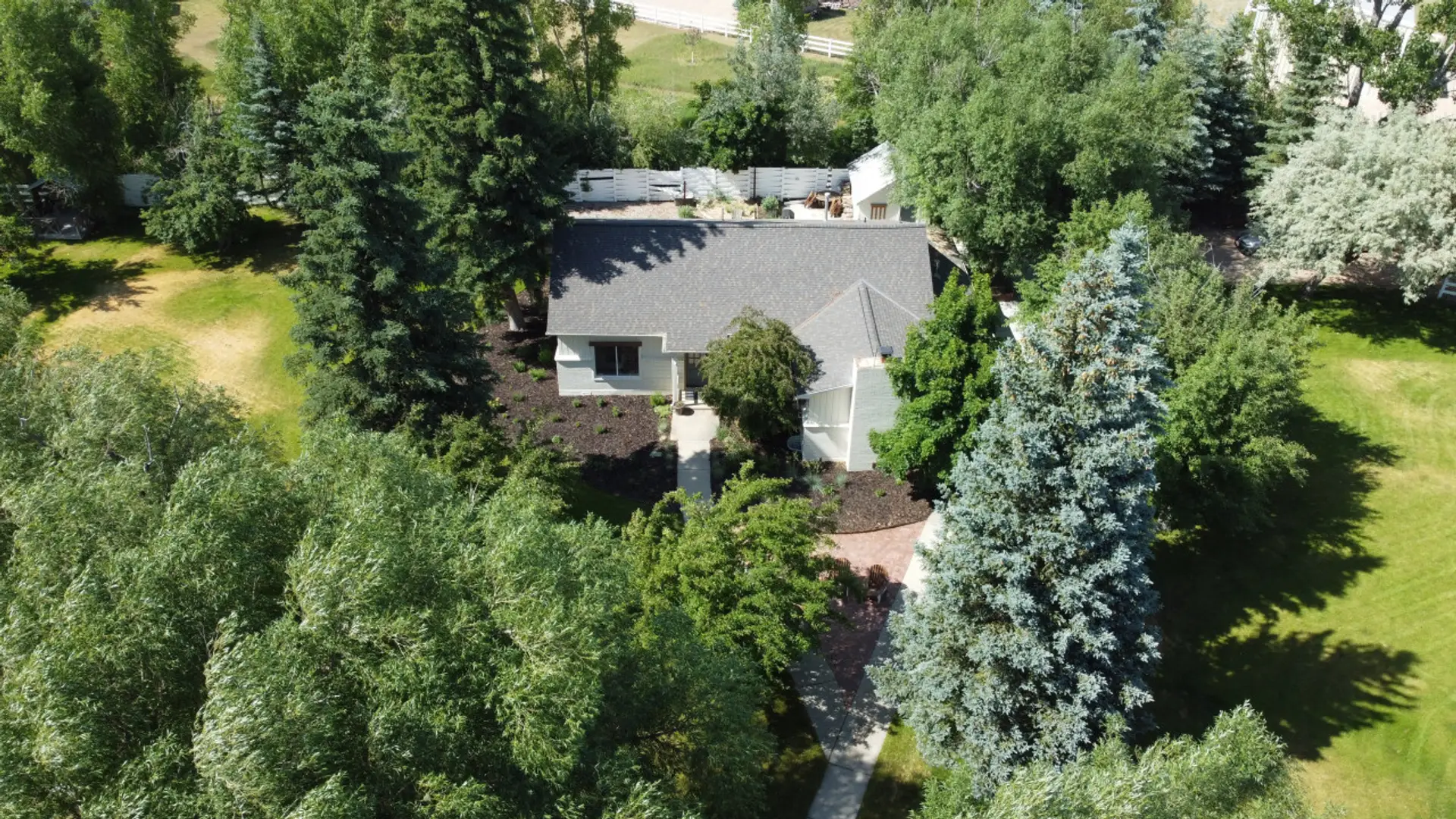 Aerial view capturing the house from the opposite side, set amidst a backdrop of trees and extensive green spaces.