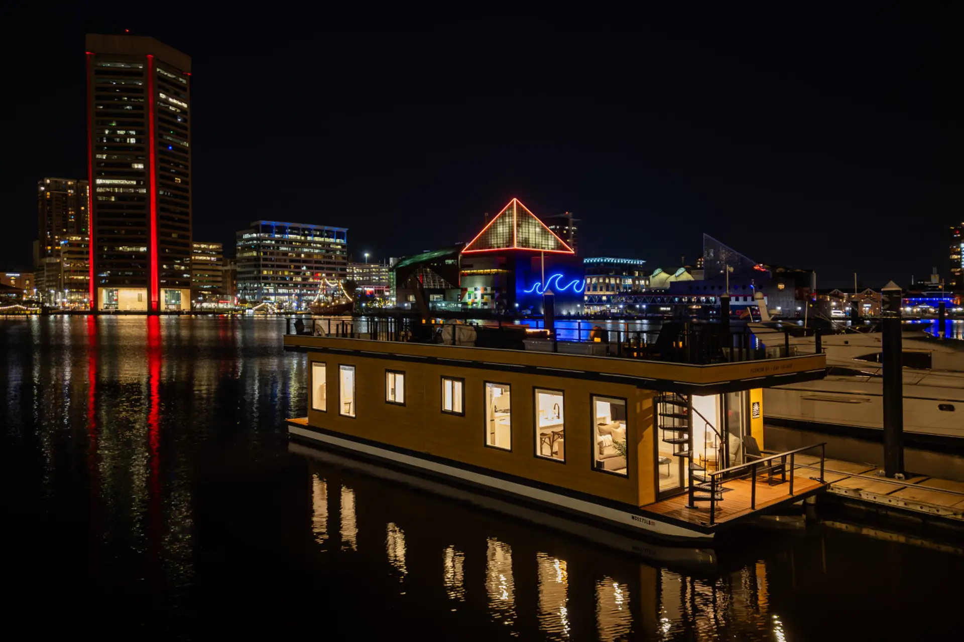Bay Escape docked in the Inner Harbor at night, with the iconic Baltimore World Trade Center and National Aquarium's neon glow reflecting on the water.