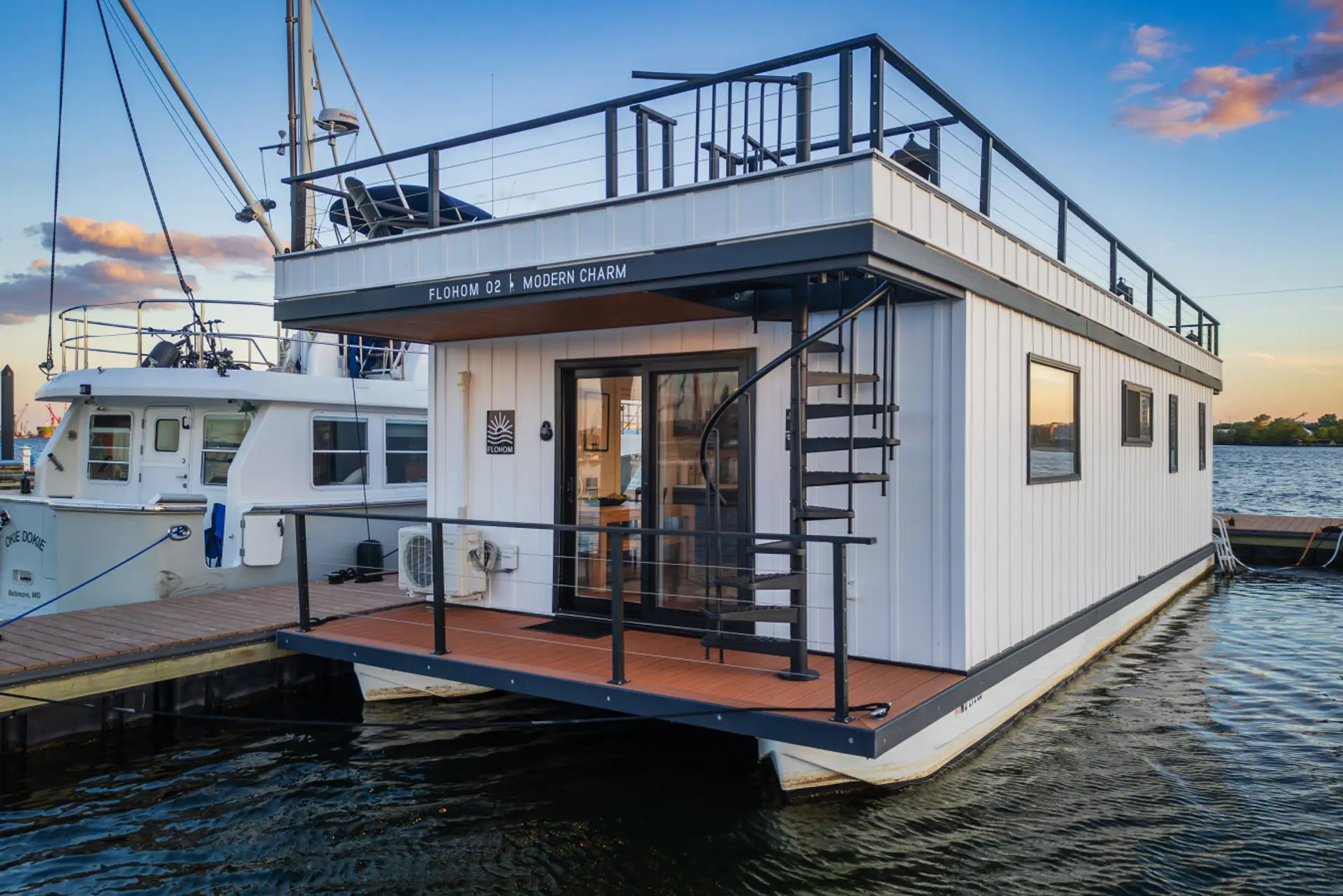 Modern Charm docked at Lighthouse Point Marina in Canton at sunset, with the spiral staircase leading to the rooftop and warm interior lights glowing from within.