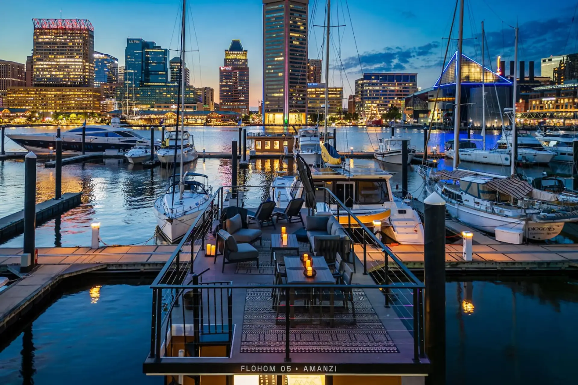 Amanzi docked at Inner Harbor Marina at twilight, with the Federal Hill skyline reflecting across the water and the rooftop lounge glowing under the Baltimore lights.