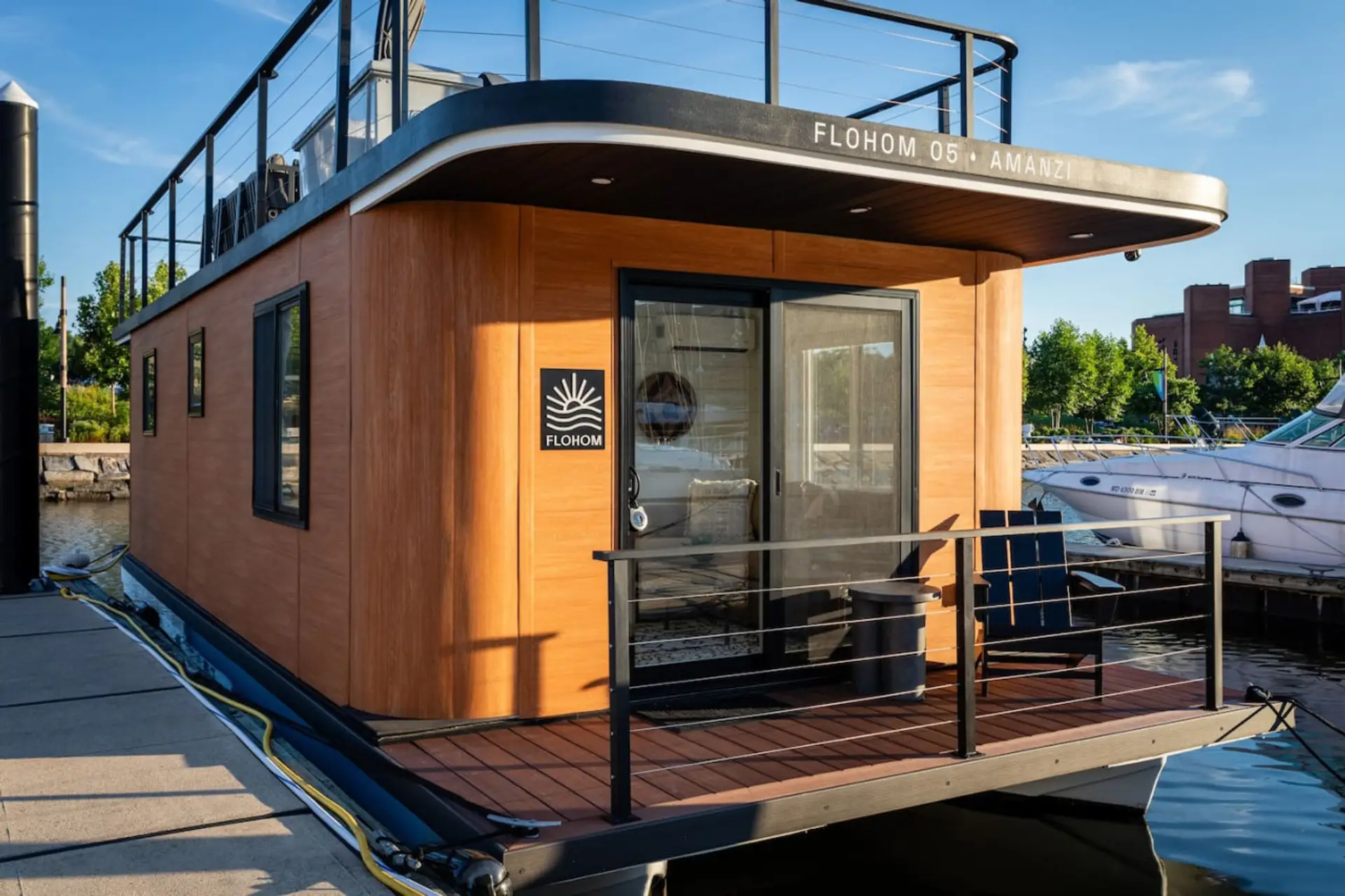 Cedar-clad exterior of Amanzi at golden hour, docked at Inner Harbor Marina with the aft deck Adirondack chair facing the boardwalk and downtown Baltimore.