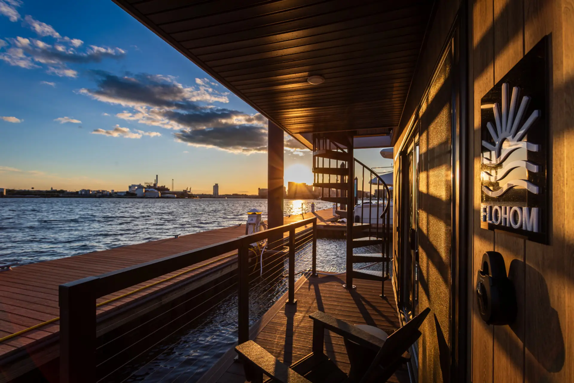 Aft deck of Harbor Hideaway at sunset, with the spiral staircase to the rooftop and the Patapsco River glowing golden across the Canton waterfront.