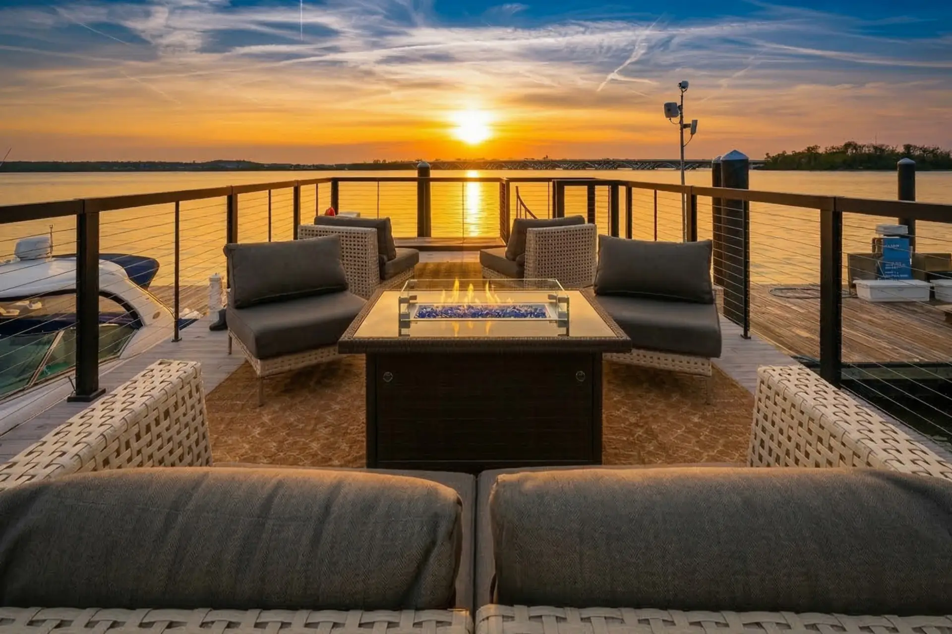 Victoria Mae's rooftop fire pit lounge at sunset, with the Potomac River glowing golden across the horizon and the Woodrow Wilson Bridge silhouetted in the distance.