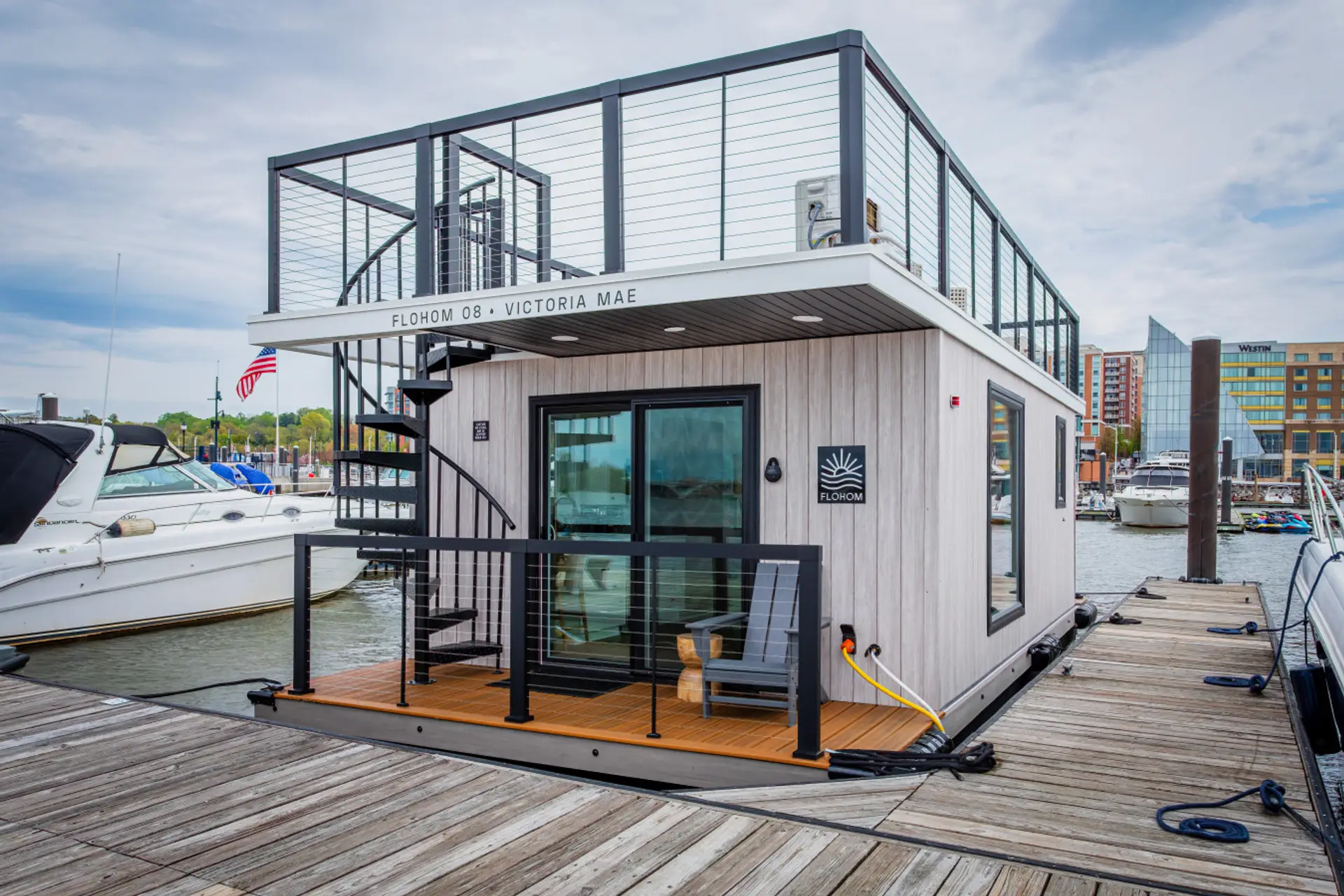 Victoria Mae docked at National Harbor Marina, with a spiral staircase leading to the rooftop deck and the National Harbor waterfront in the distance.