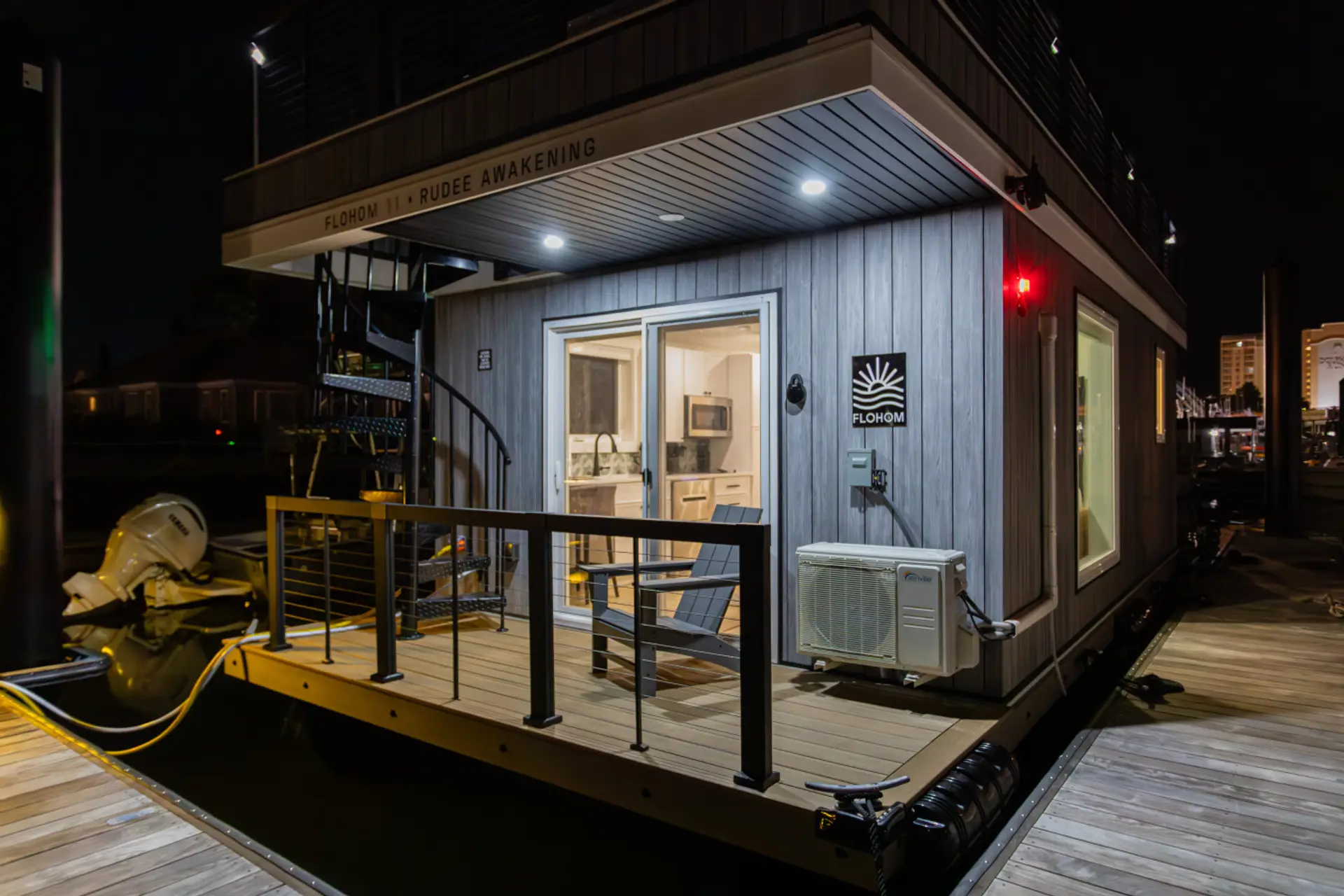 Nighttime arrival view of the private entry deck on Rudee Inlet, softly lit beside an Adirondack chair and spiral stairs leading up to the private rooftop lounge.