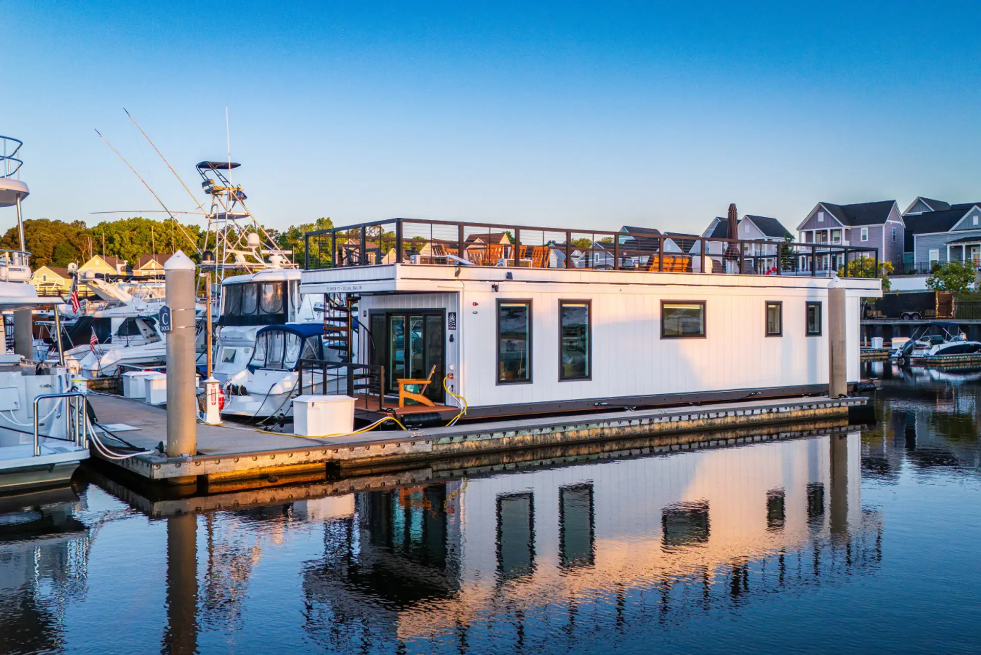 Selah Sailor in full morning light at Barefoot Marina, with the rooftop deck, open waterway, and the property's reflection stretching across the still water below.