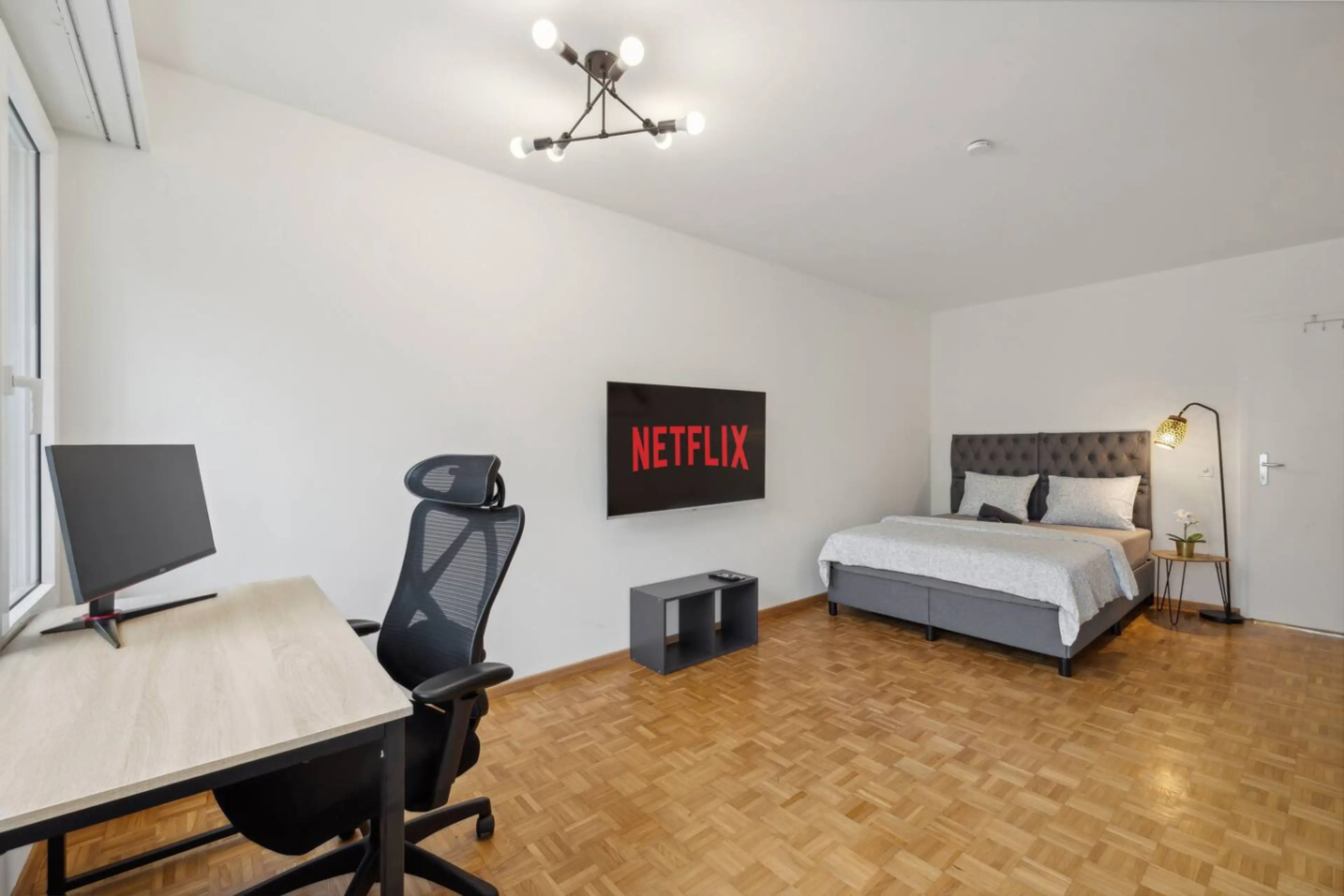 Spacious bedroom with box-spring bed, 55" Netflix TV & full home office setup.