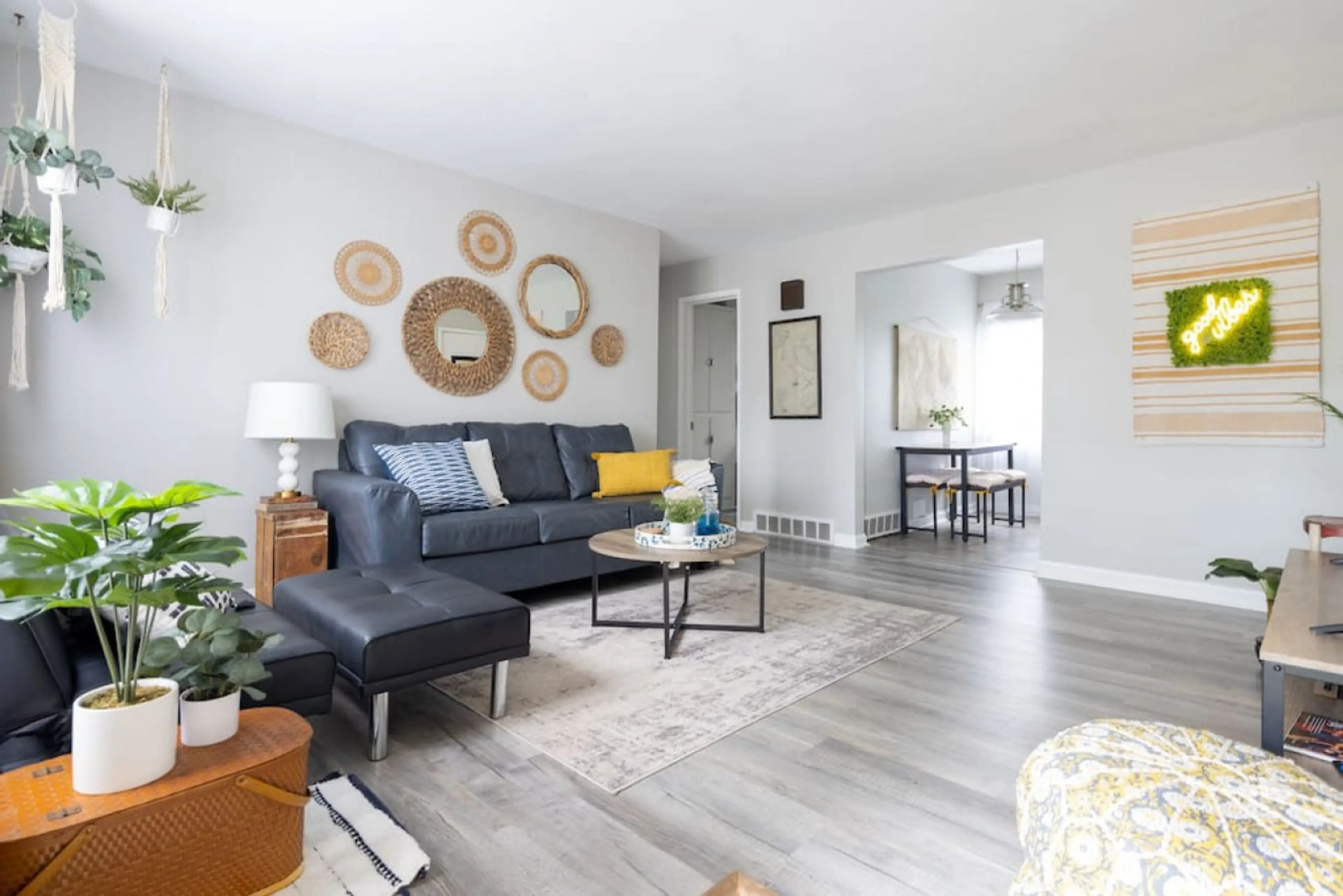 Airy open-concept living room with a navy sofa, matching ottoman, and round wood coffee table layered over rugs. Boho wall décor and hanging planters tie the seating area together for seamless relaxation 🌿🛋️