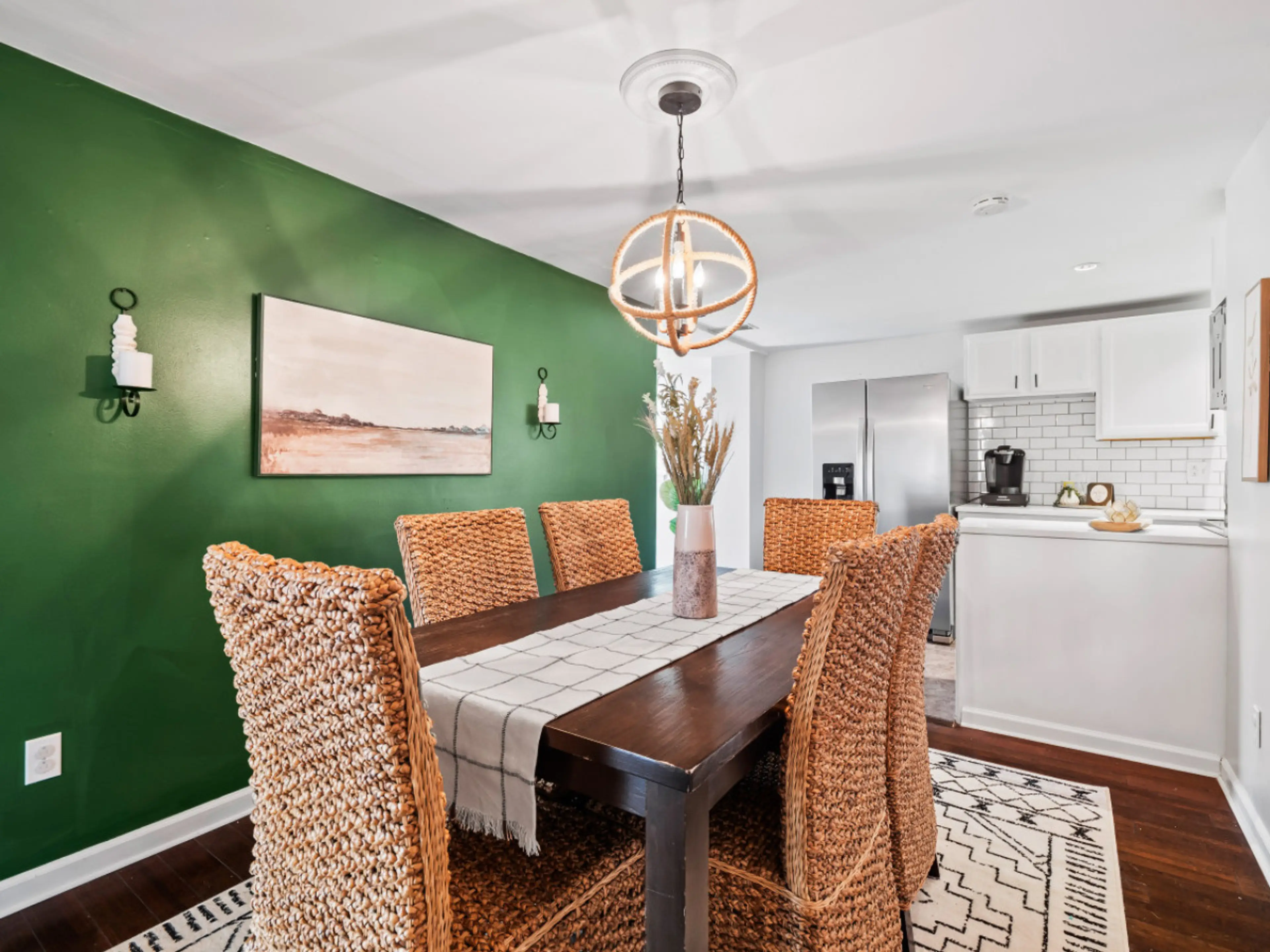Dine in style in this earthy, modern space 🌿✨ With its rich green accent wall, woven chairs, and warm wood tones, this dining area is perfect for gathering over meals, games, or conversation. Plus, easy access to the kitchen! 🍽️