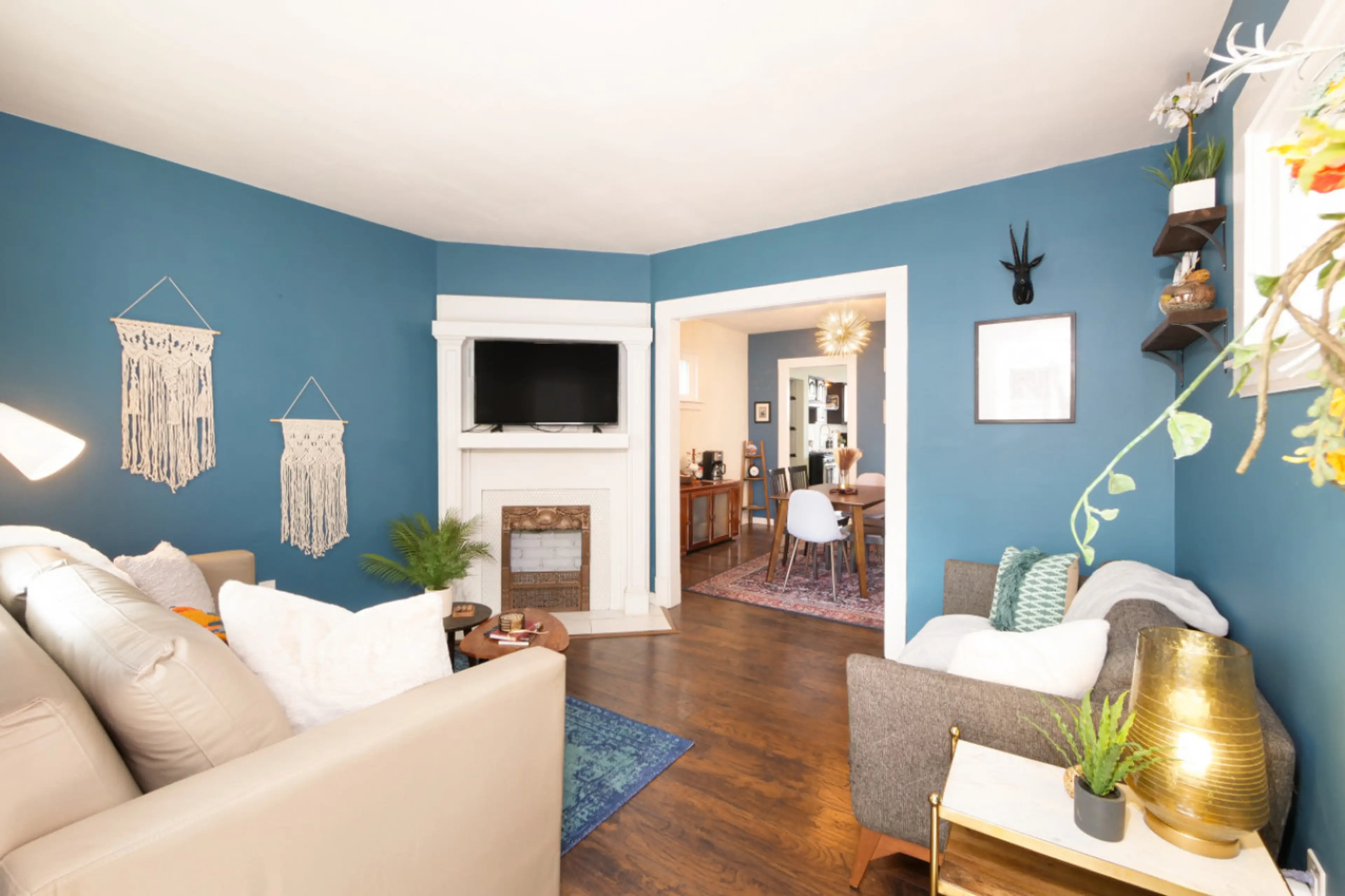 Relax in this bright, boho-inspired living room with bold blue walls, comfy seating, and stylish decor. Perfect for streaming your favorite shows or catching up over coffee! 📺✨