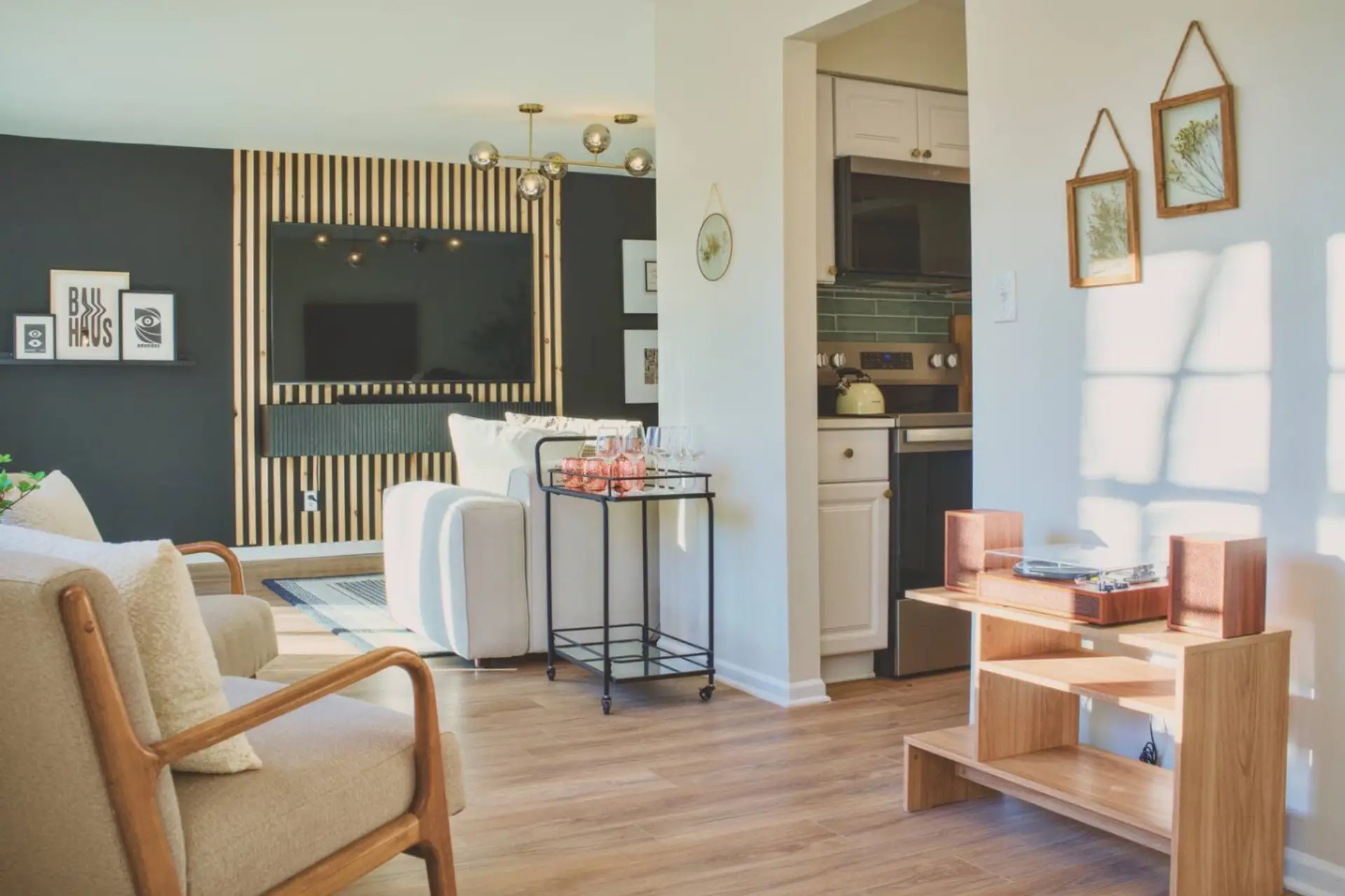 From the sofa, string lights glow against the wood-slat wall while the open layout carries straight through to the kitchen, so nobody's stuck cooking alone.