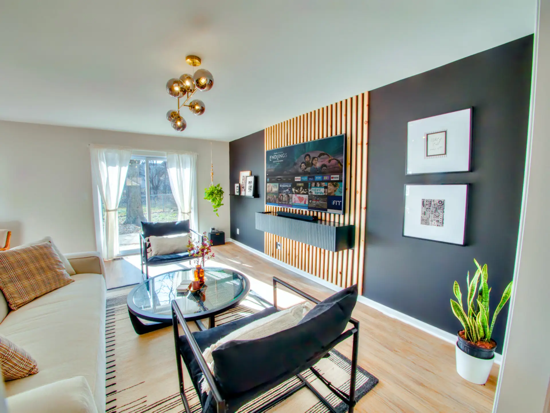 Step into the living room and you'll want to stay awhile: a moody navy accent wall wrapped in wood slats, a gold sputnik chandelier overhead, and black leather seating built for sinking in after a long day.