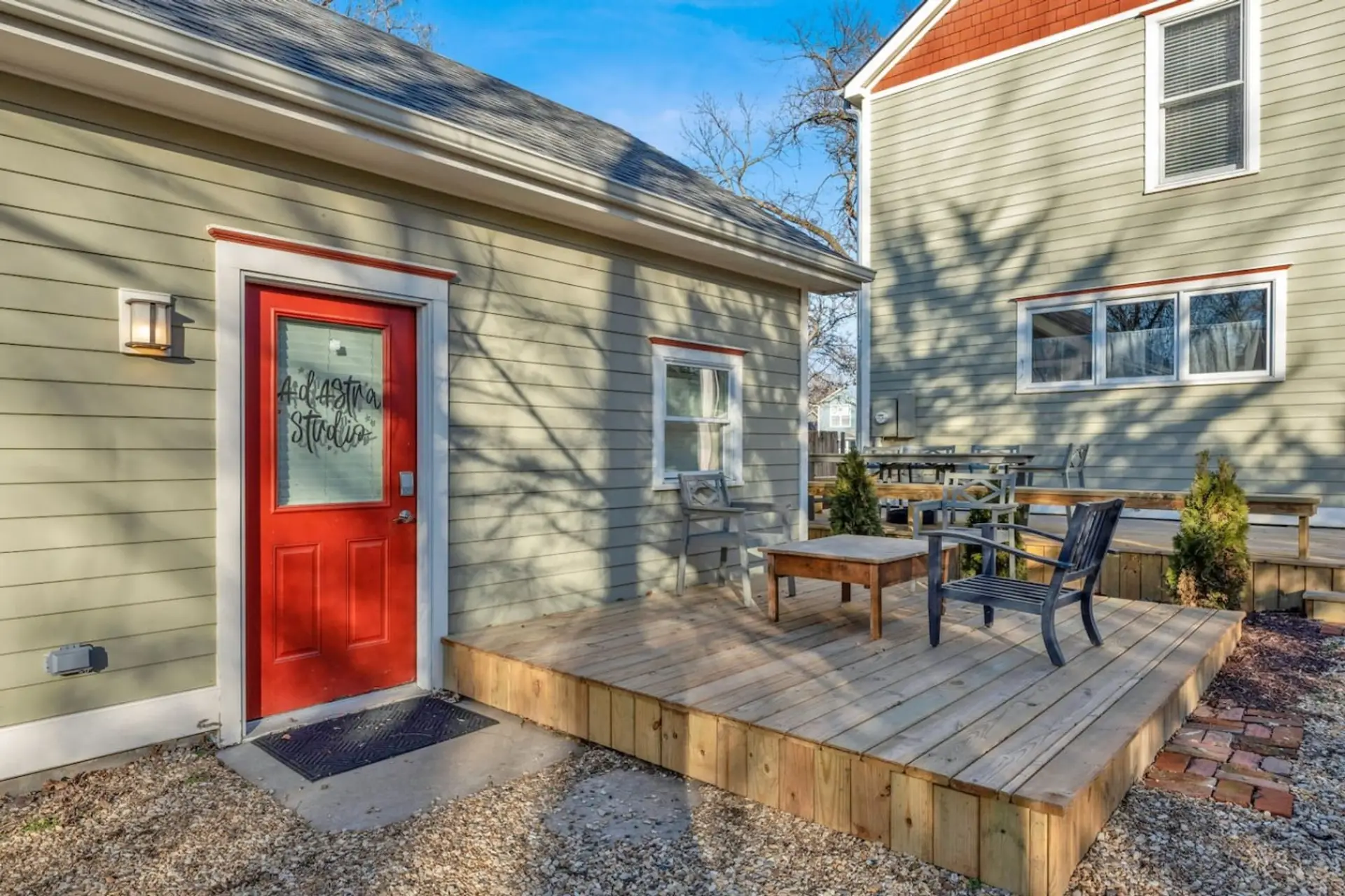 Step up to your own red door, hand-lettered with the studio's name — a small wood table and two chairs on the deck invite you to sit a minute before you even get your bags inside.