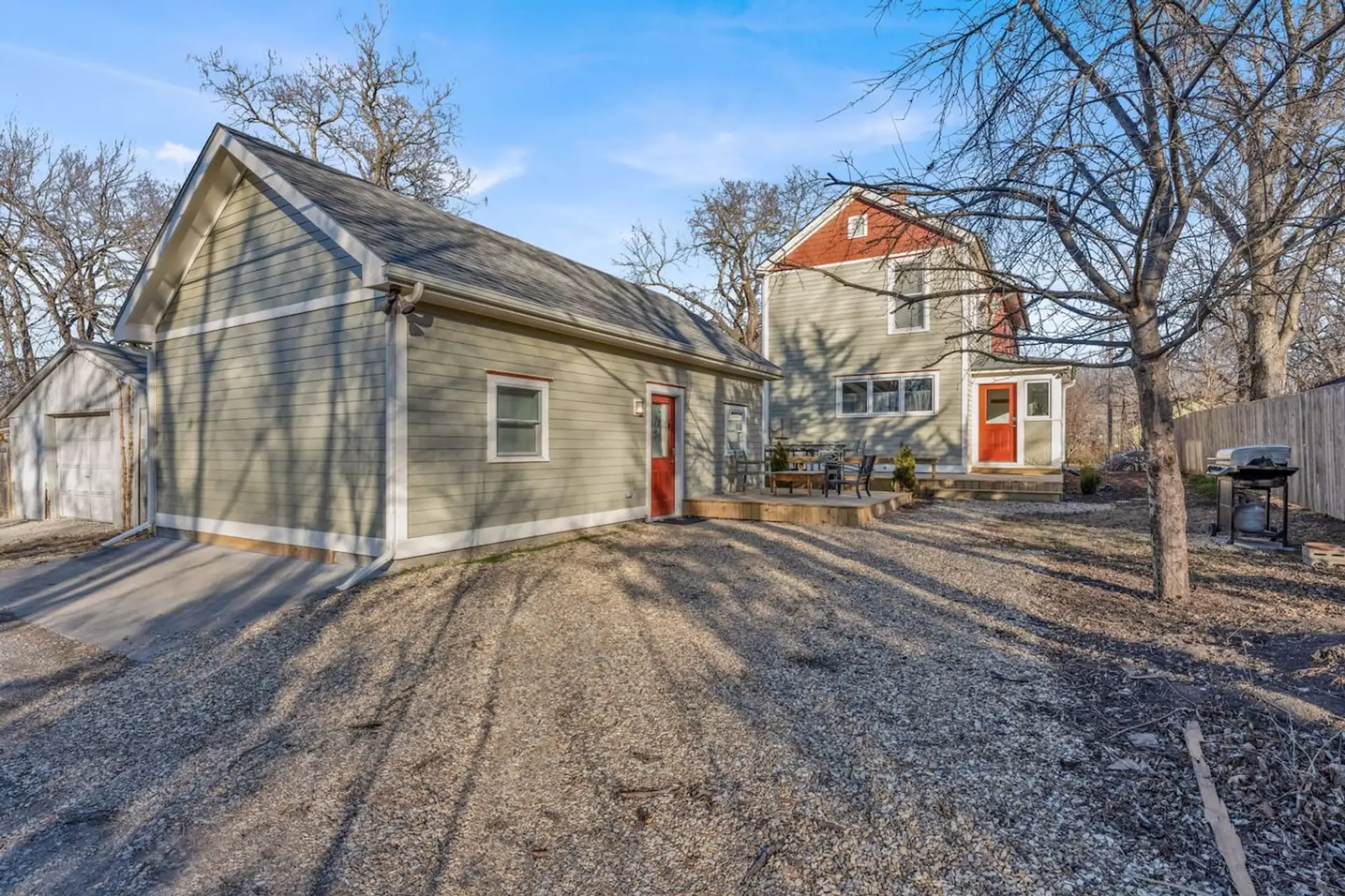 From the gravel drive, you'll spot the detached garage, the studio's gabled roofline, and the main house's red trim glowing behind bare branches — quiet, tucked-away Lawrence living.
