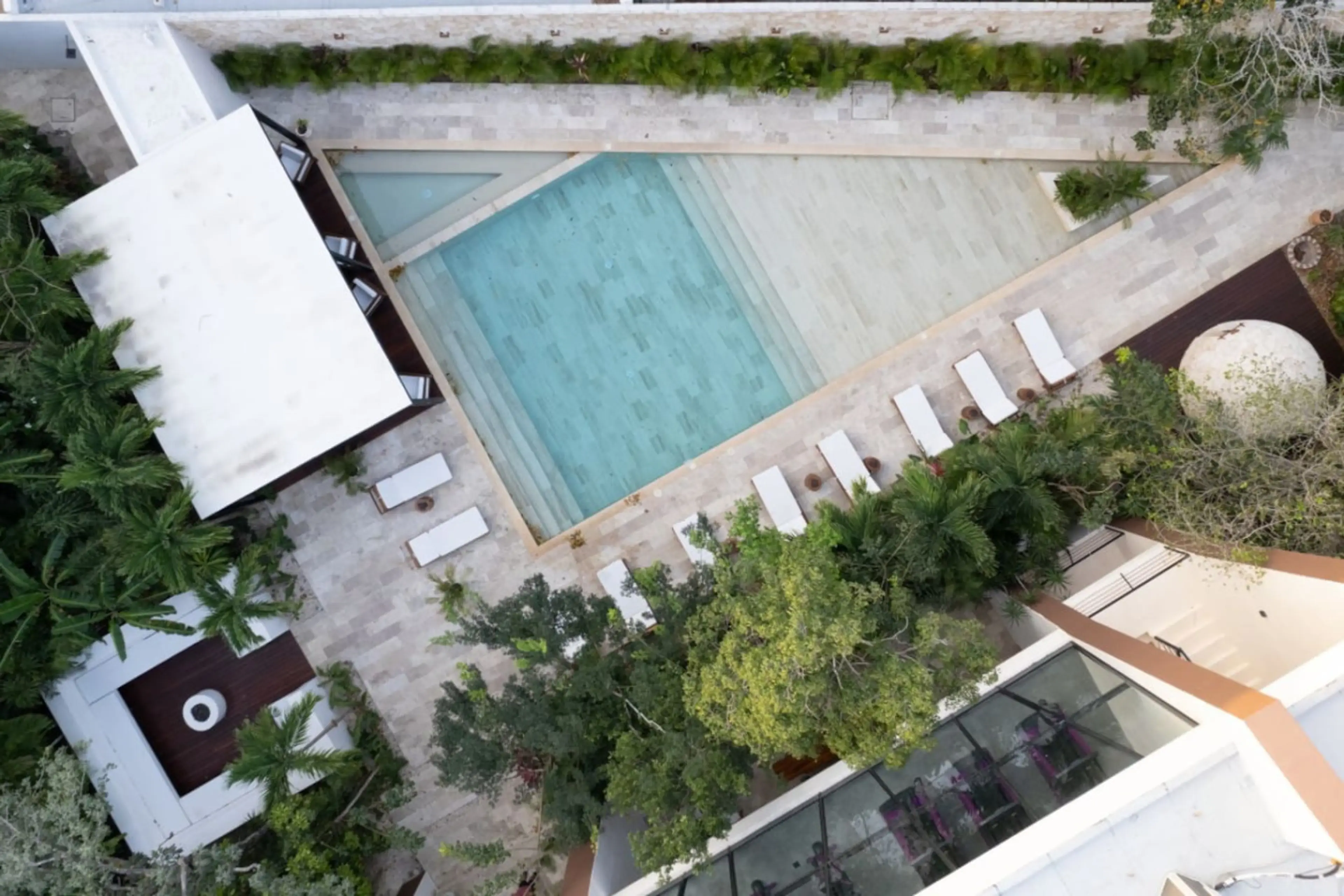 A bird’s-eye view of a peaceful pool area featuring lounge chairs, shaded beds, tropical trees, and a temazcal—an ideal place to relax and embrace the tranquil Tulum vibe.