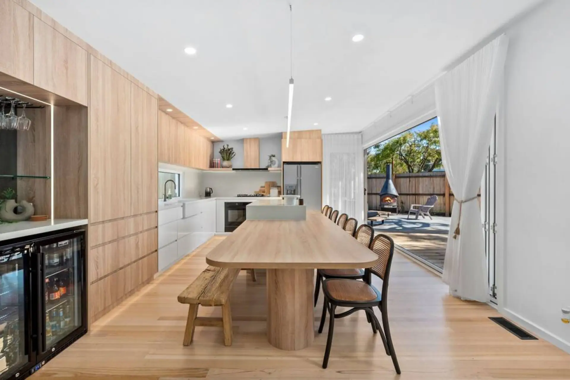 This stunning open-plan kitchen and dining space features sleek timber finishes, a wine fridge, and seamless indoor-outdoor flow to a sun-drenched courtyard with a chiminea