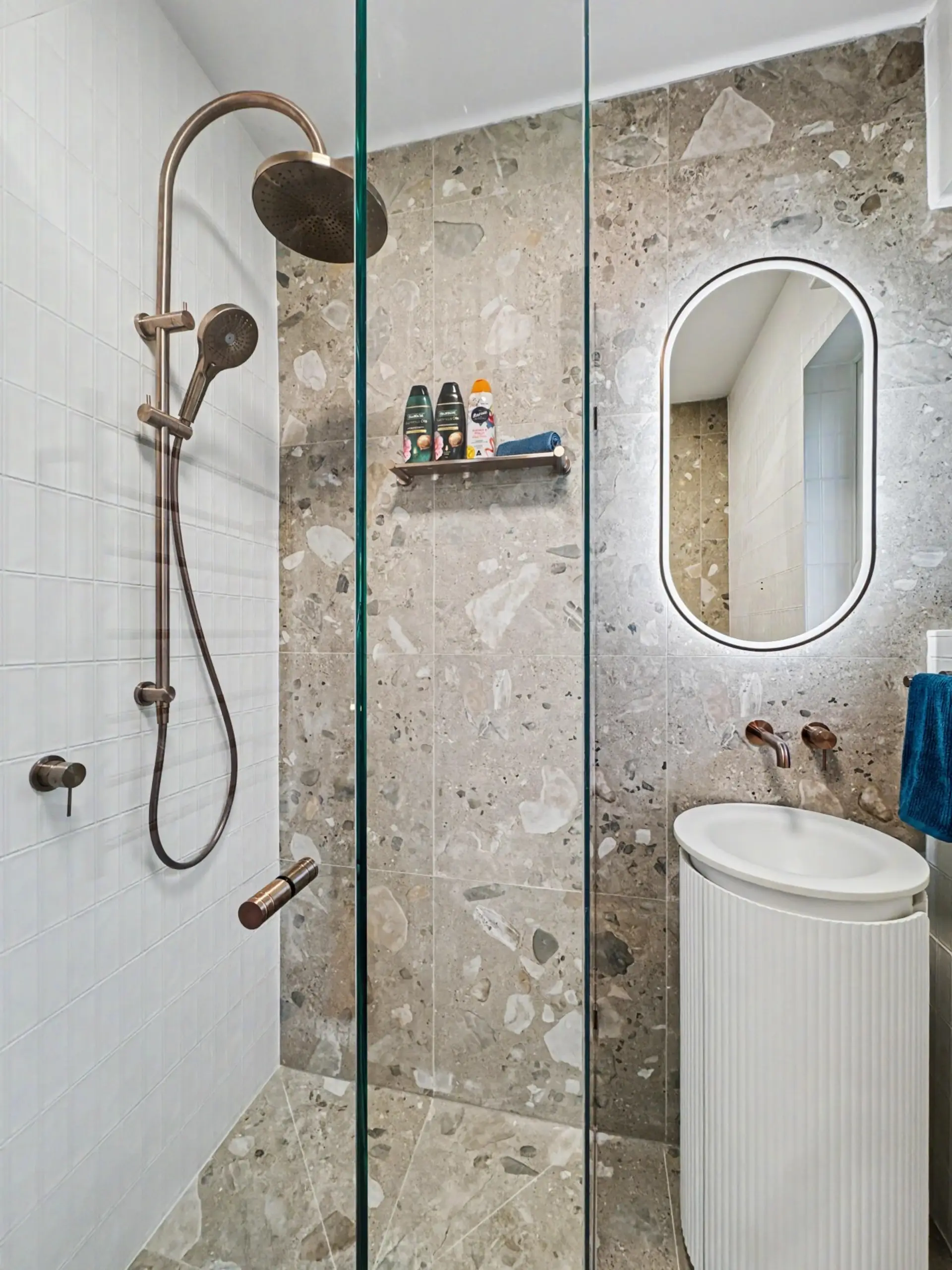 Enjoy a spacious walk-in shower with both rainfall and handheld shower heads, surrounded by beautiful stone and brushed bronze finishes