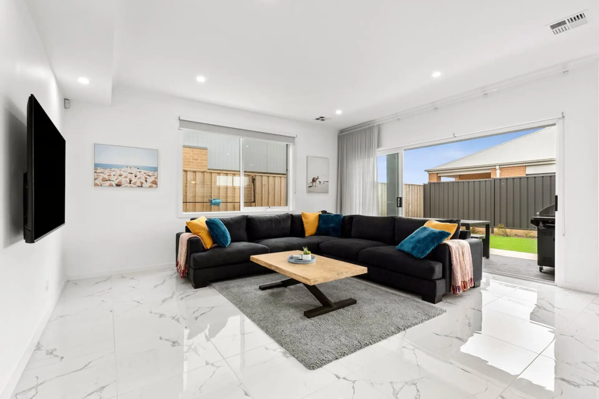 Kick back in this bright and stylish lounge room featuring a huge comfy couch, smart TV, and sliding doors that open out to the backyard for easy indoor-outdoor living