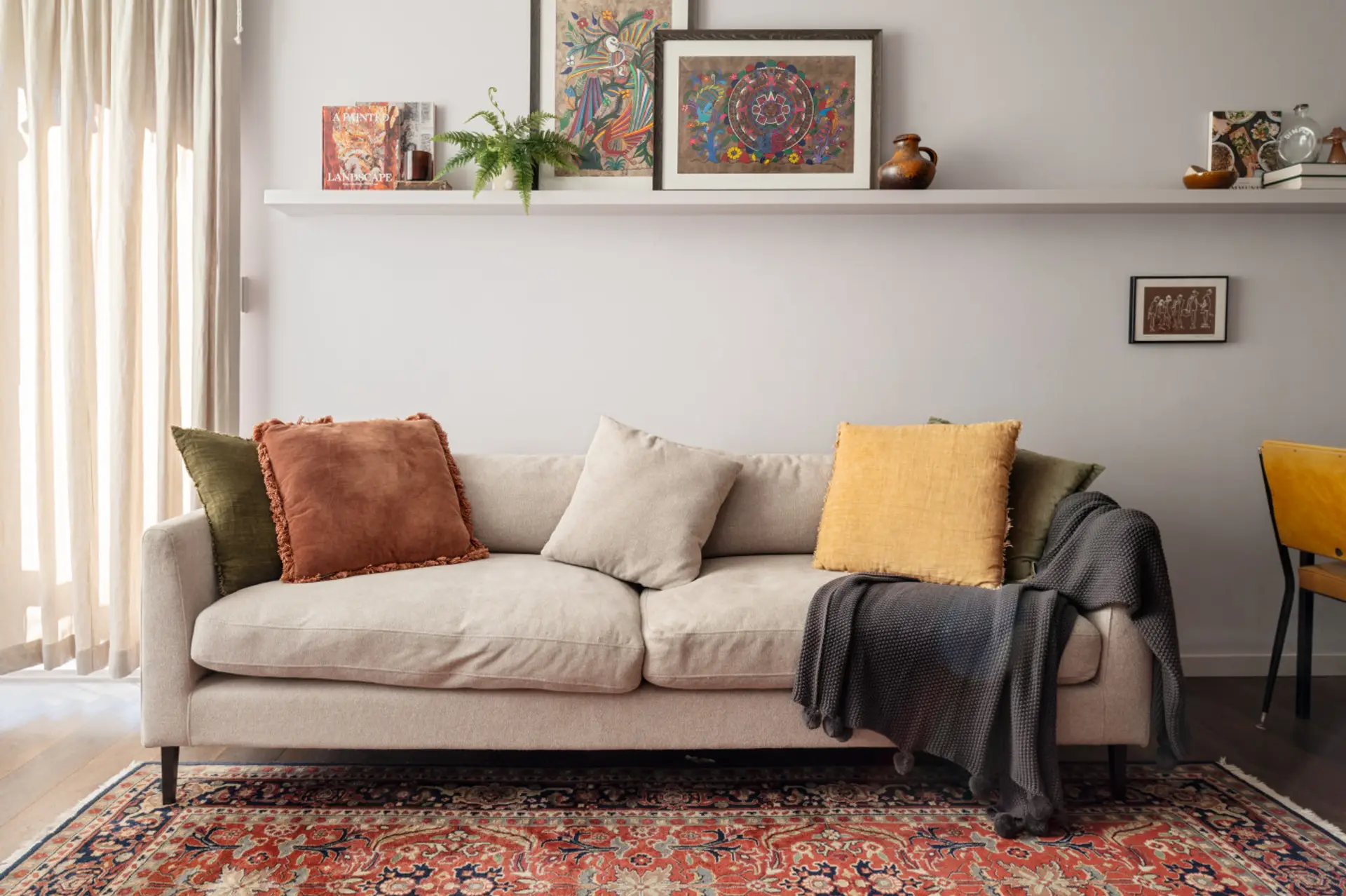 Relax in the inviting living room, styled with a plush neutral sofa, vibrant cushions, a vintage rug, and curated artwork for a warm, homely feel
