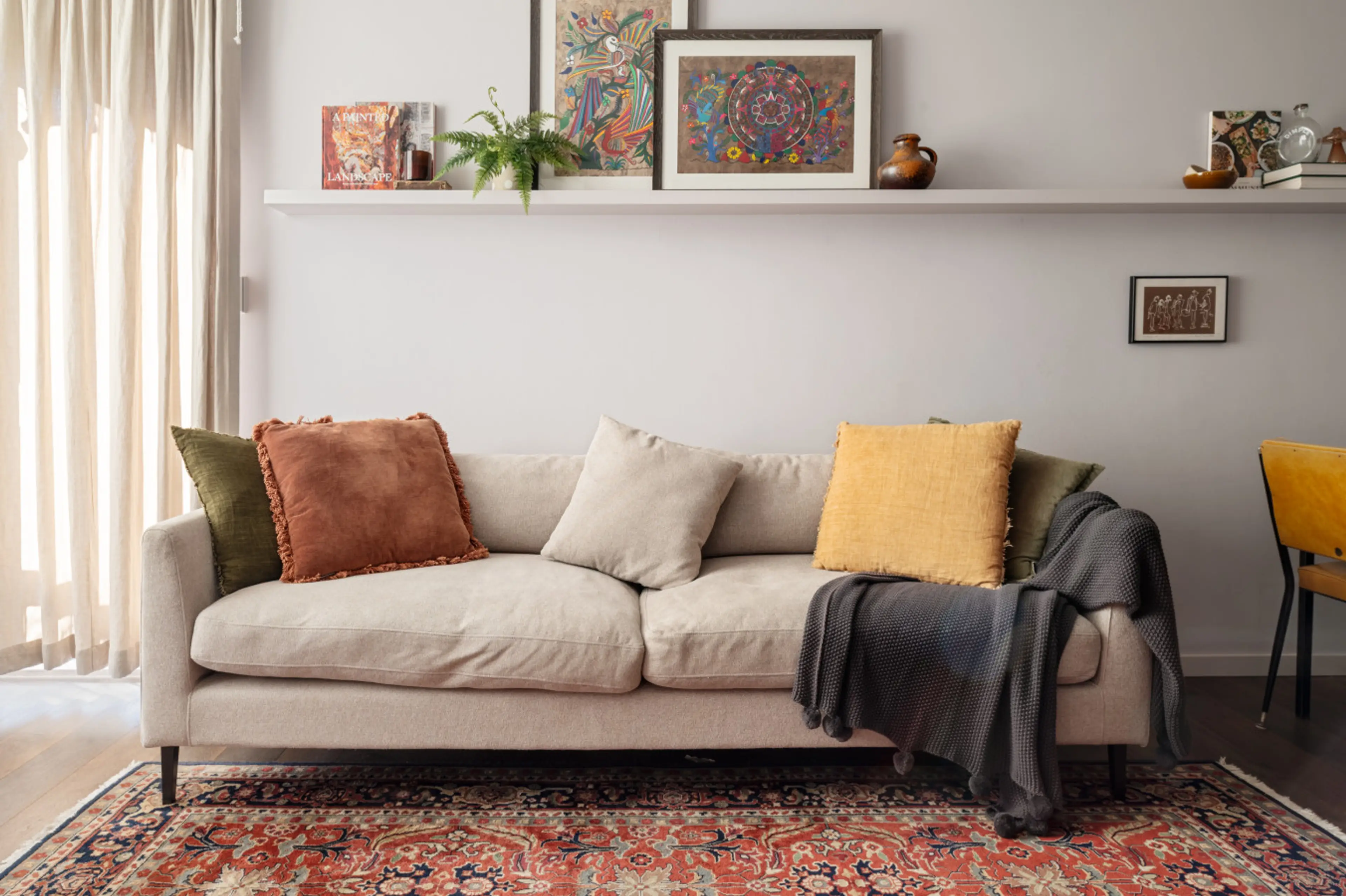 Relax in the inviting living room, styled with a plush neutral sofa, vibrant cushions, a vintage rug, and curated artwork for a warm, homely feel