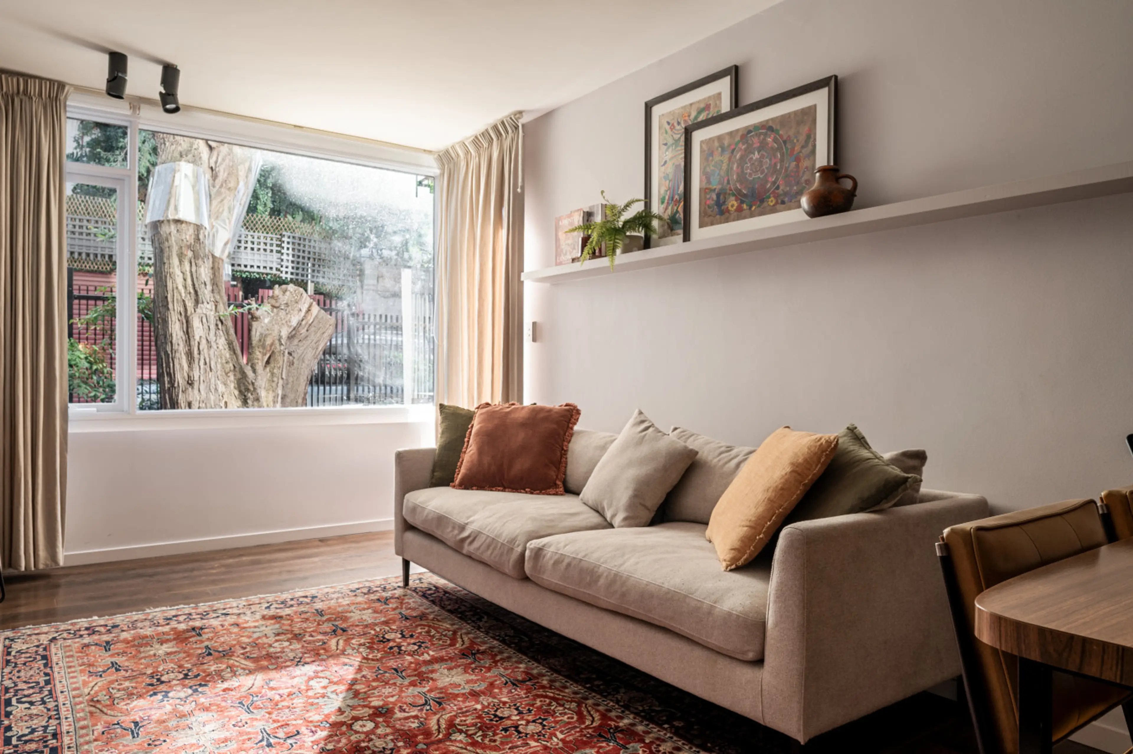 Enjoy a peaceful outlook from this sun-filled living room, complete with a comfy neutral sofa, colorful cushions, and a vintage-style rug for added warmth