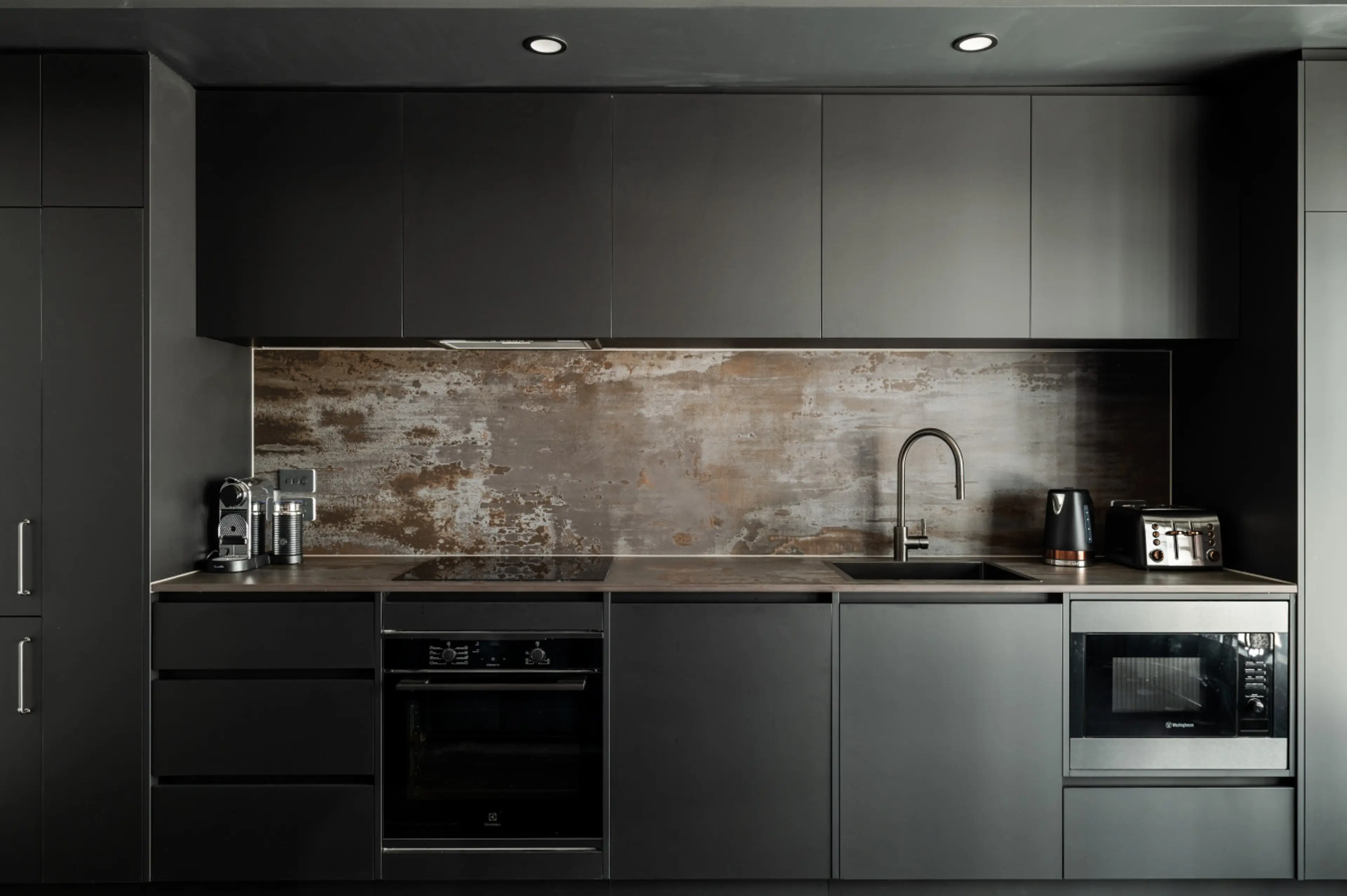 Stylish, fully equipped kitchenette featuring sleek cabinetry, quality appliances and a striking industrial-style splashback