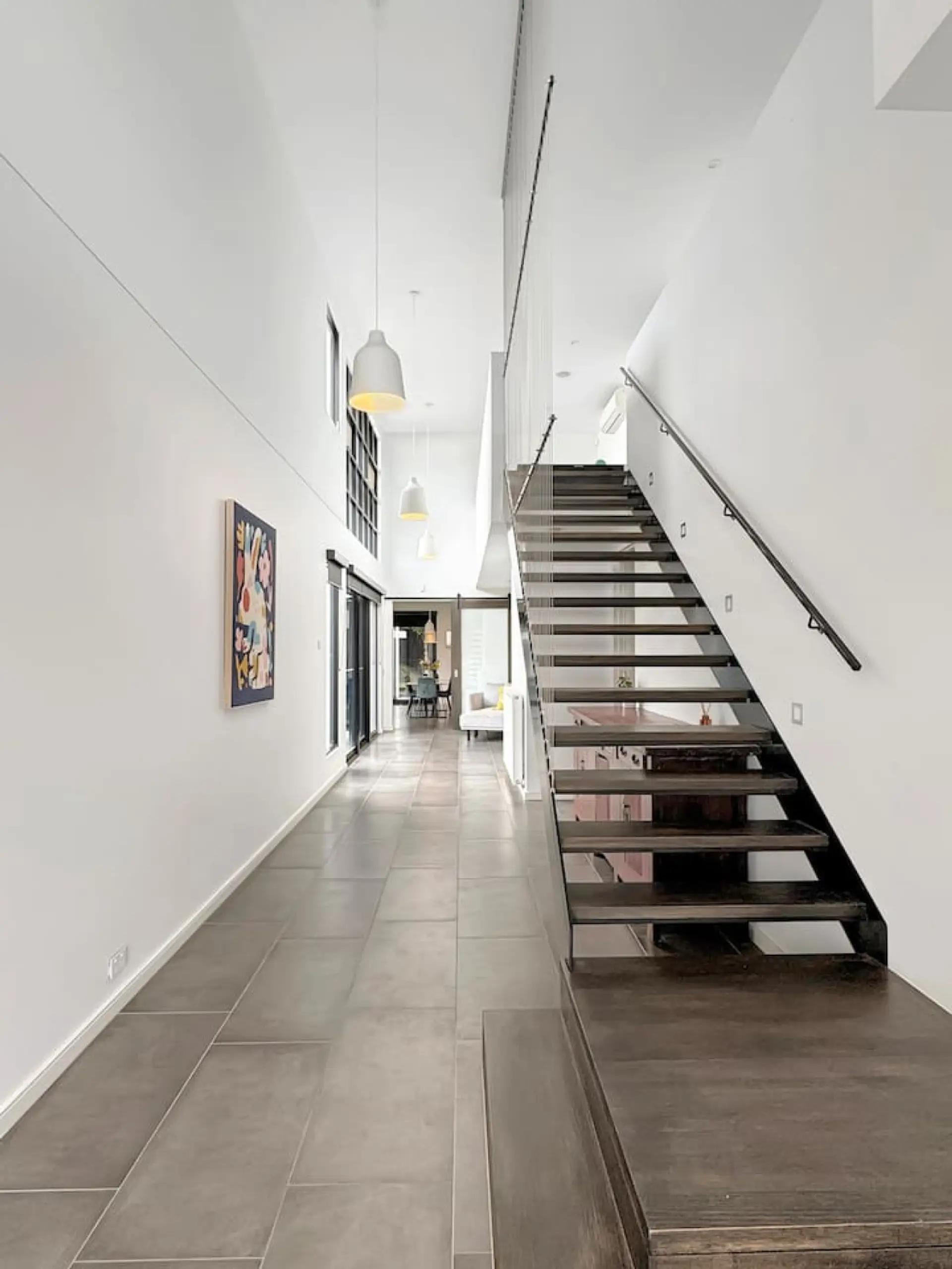 A light-filled, architecturally designed hallway with soaring ceilings, sleek tiled floors and a striking open staircase that sets the tone for this modern home