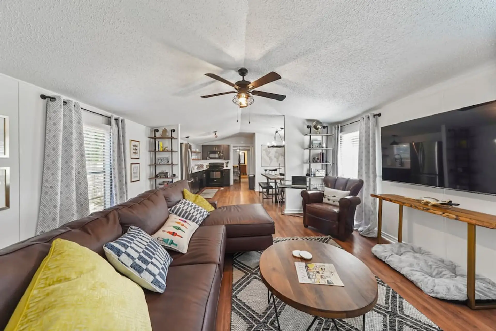 Open living room with leather sectional, 65” Smart TV, and direct access to the kitchen and dining area.