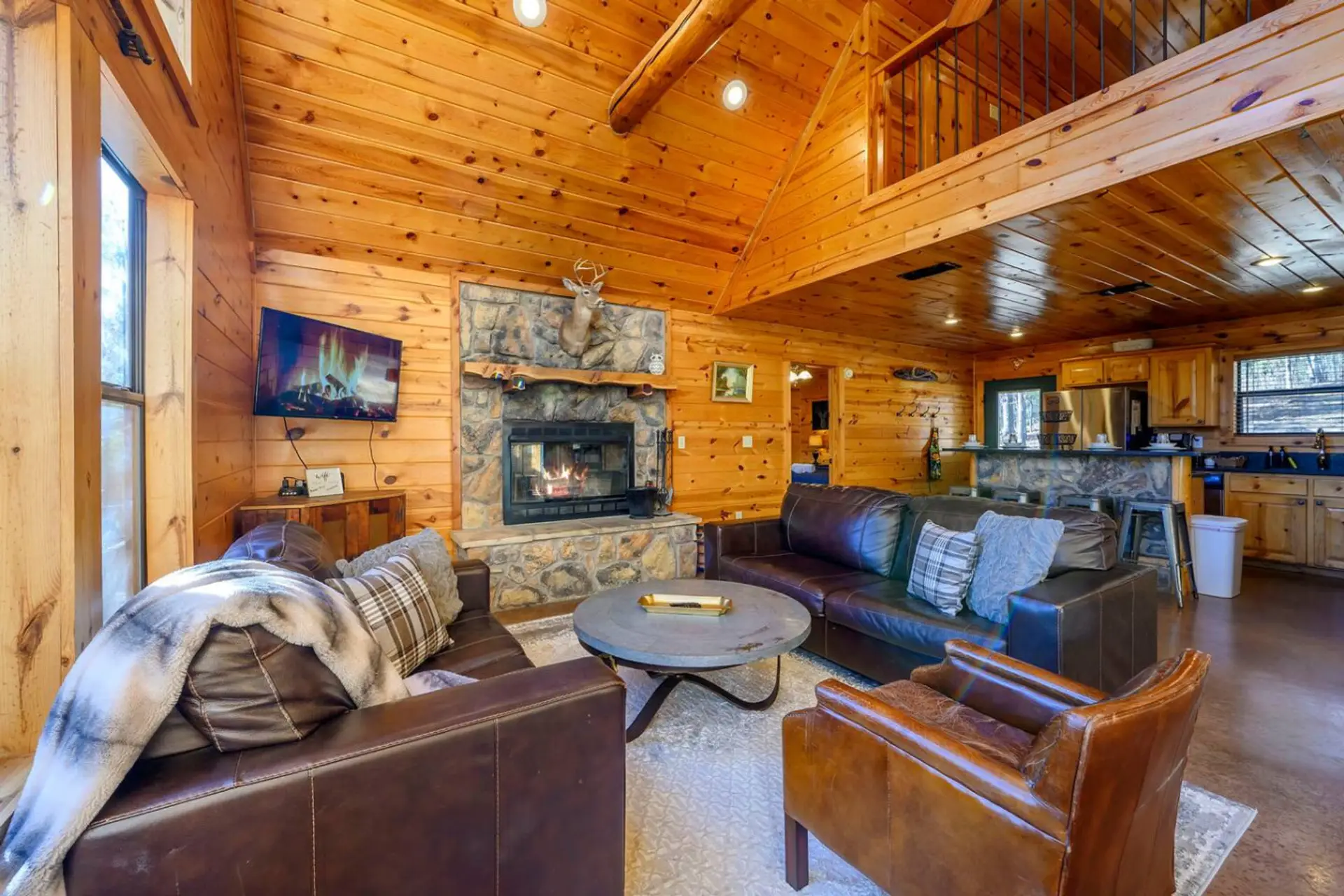 This cozy log cabin living room features a stone fireplace, leather seating, and tons of natural wood charm perfect for unwinding.
