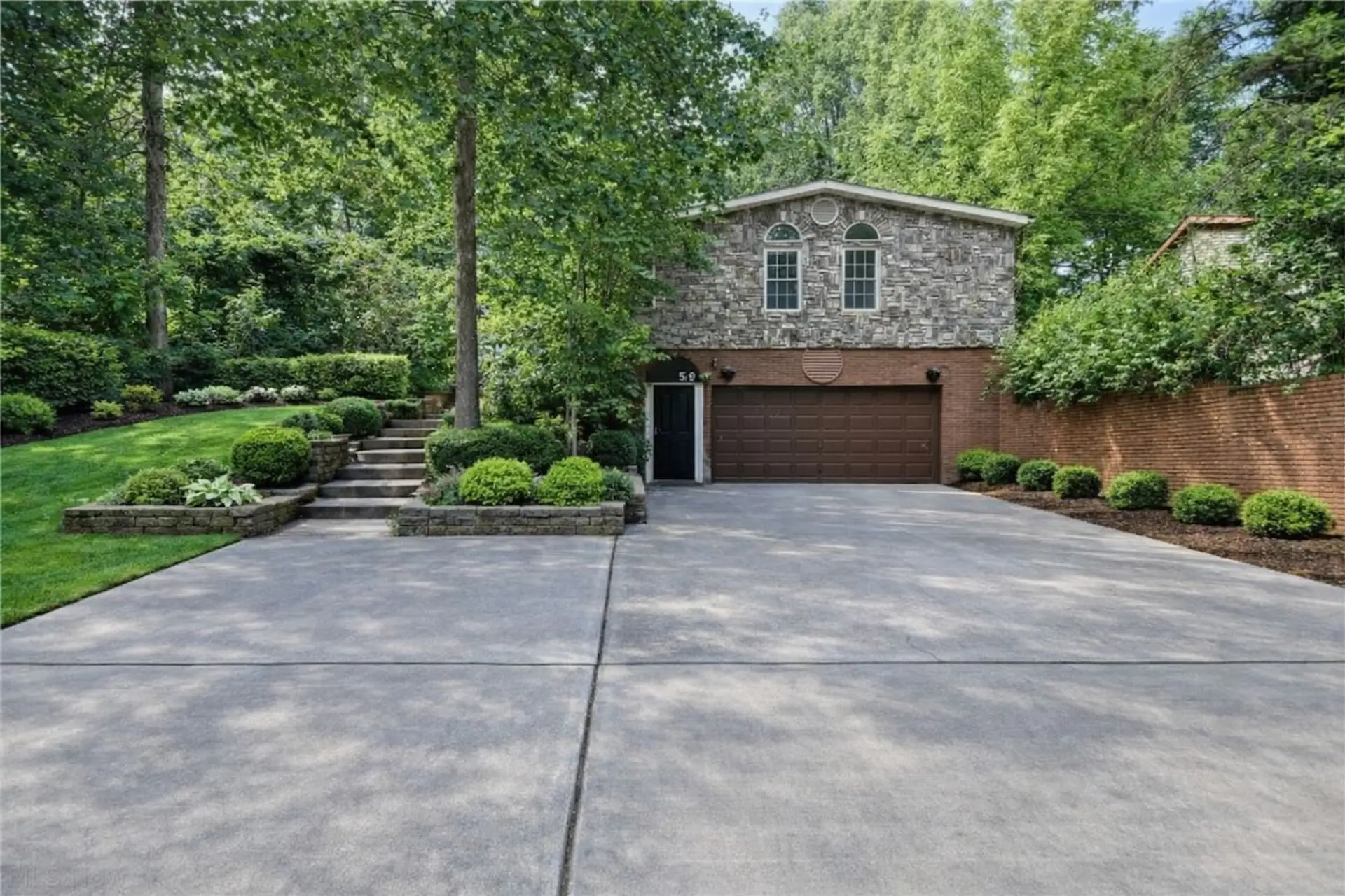 Welcome guests with an expansive driveway for easy parking, set against a beautifully landscaped facade with stone accents and lush greenery.